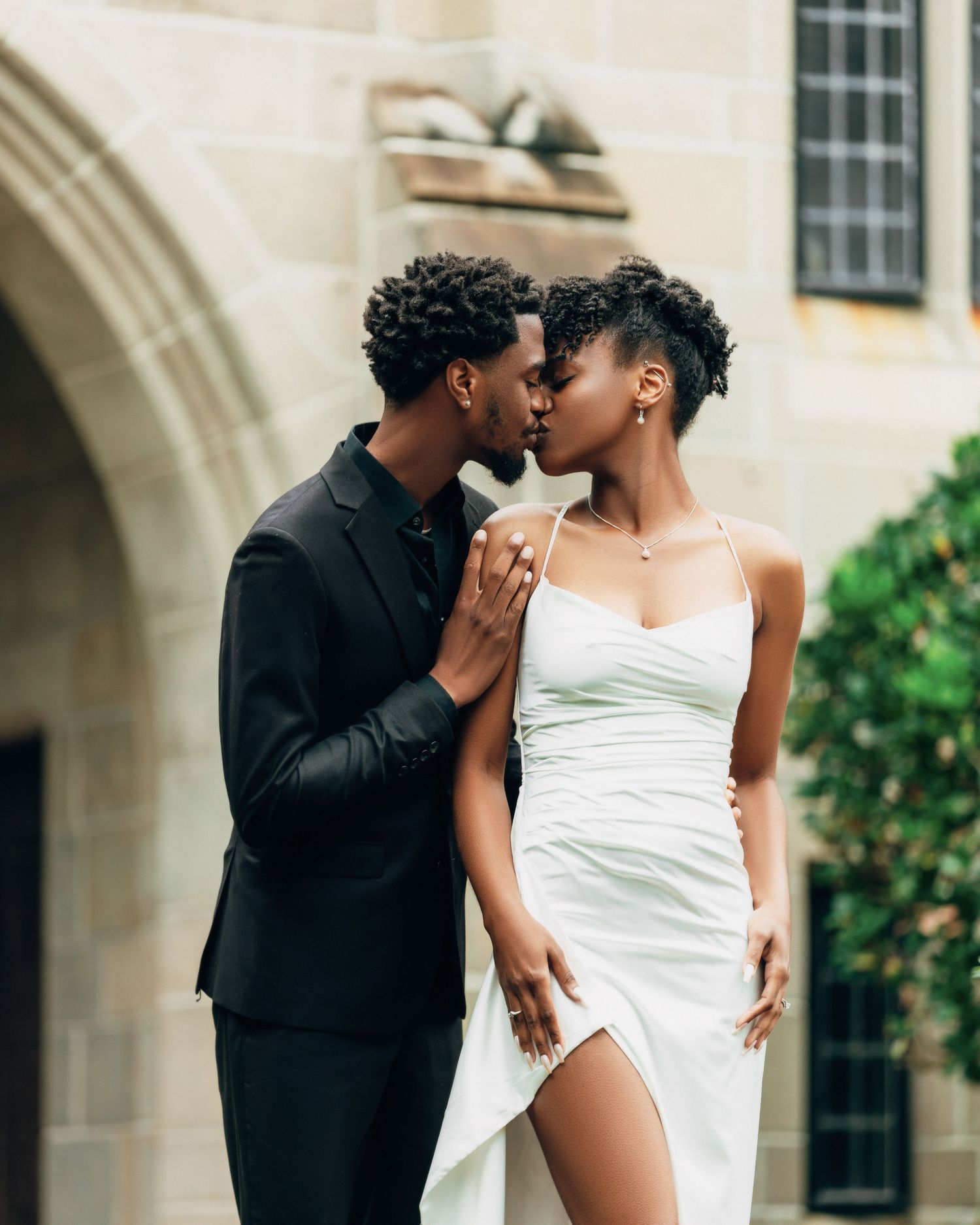 Romantic couple shares tender moments against architectural backdrop.