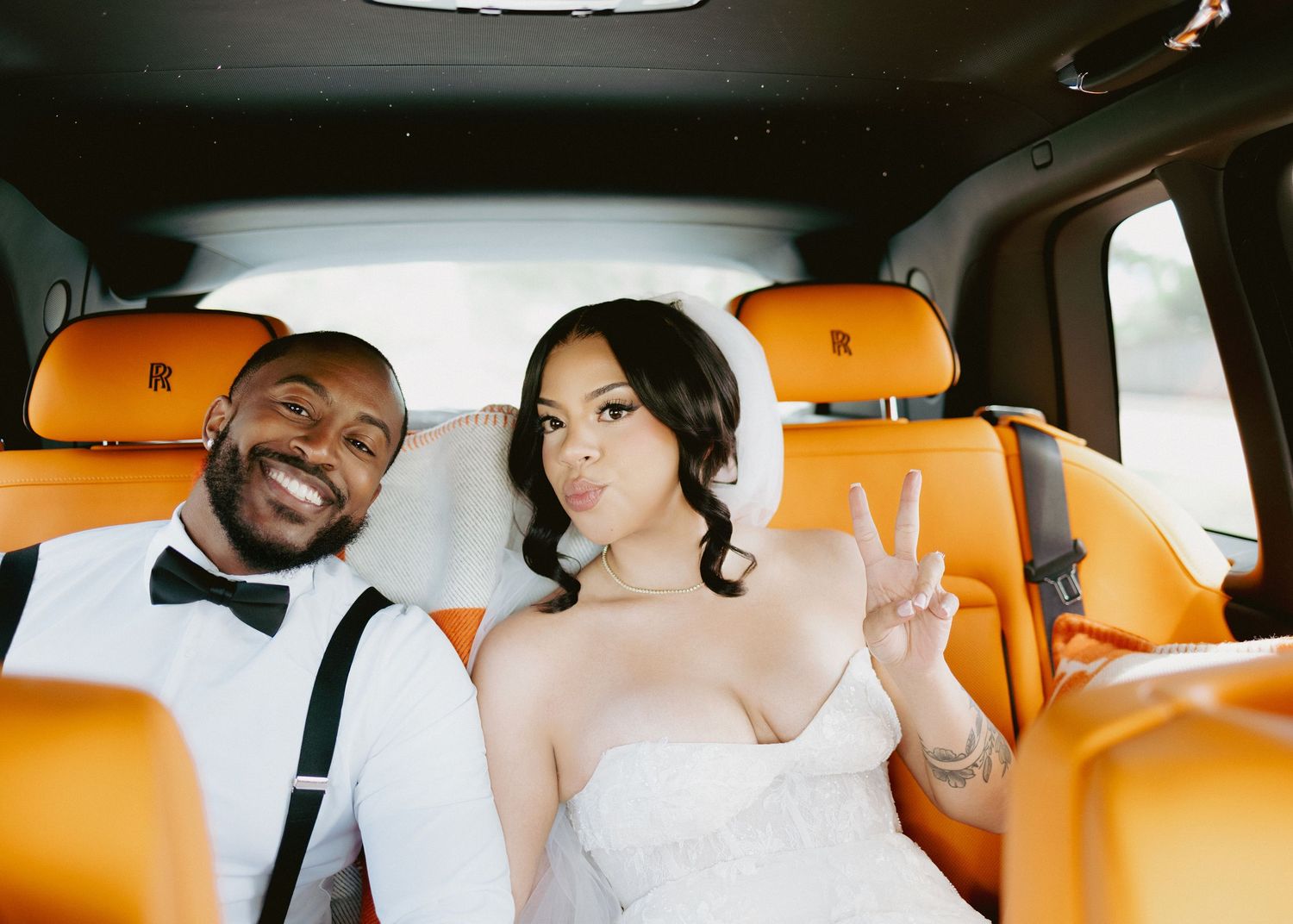 Bride and groom smiling in luxury Rolls-Royce car with tan leather interior on wedding day.