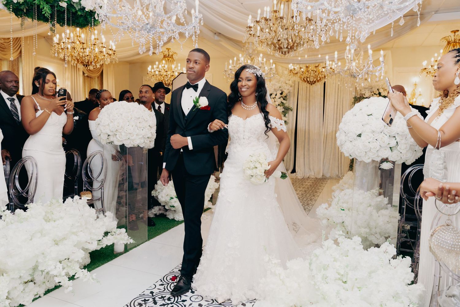 Wedding reception features grand ballroom dancing under crystal chandeliers with white floral decor.