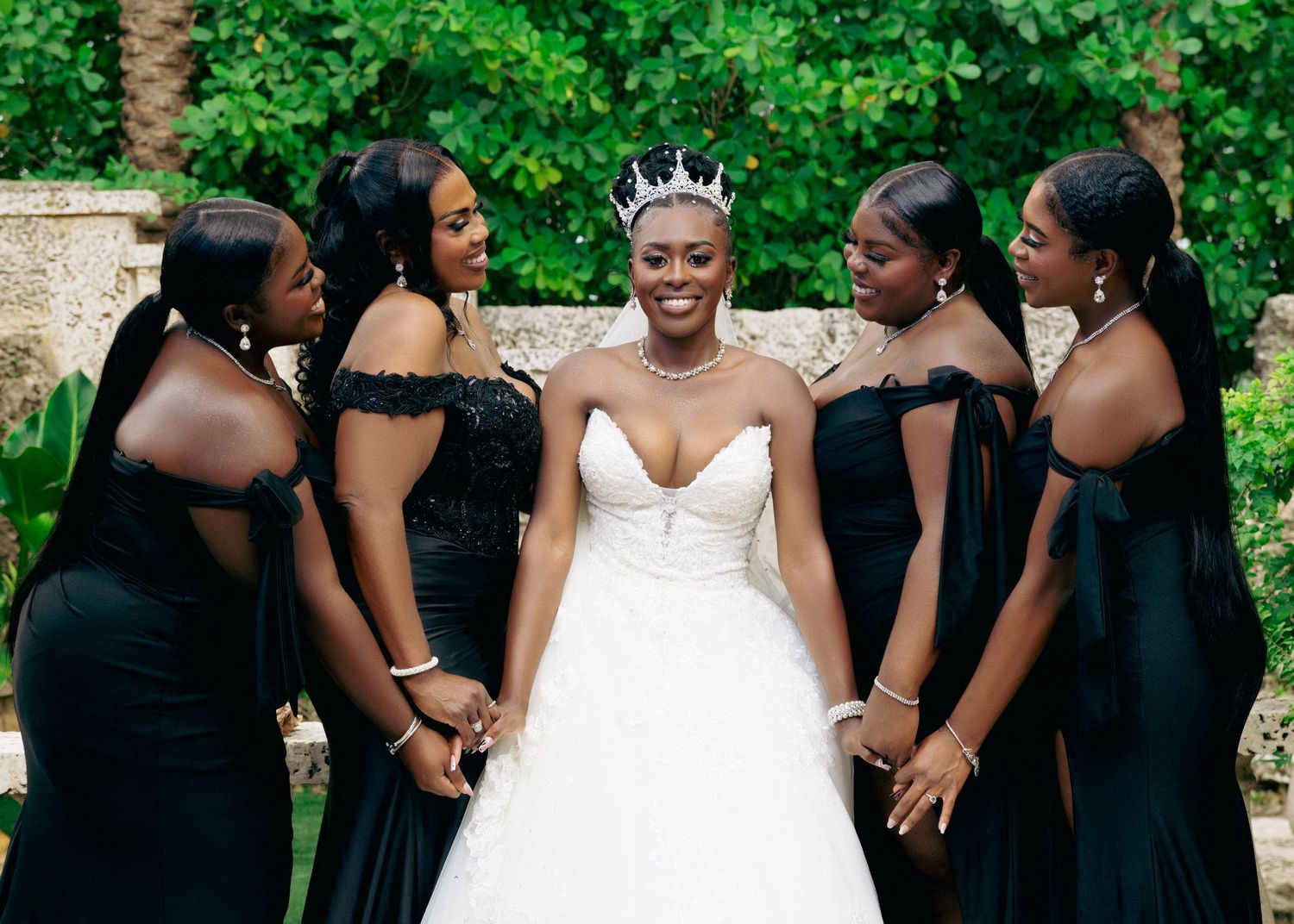 Wedding party wearing black bridesmaid dresses poses with bride in white gown.