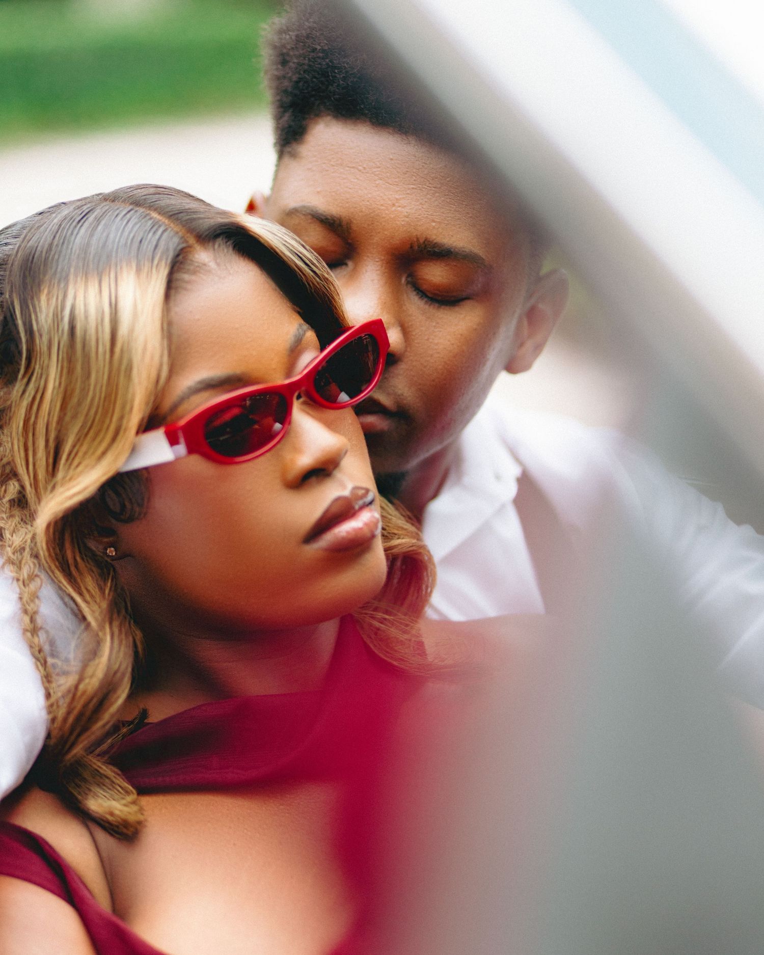A romantic couple in sunglasses embracing in a soft dreamy outdoor setting with blurred background.