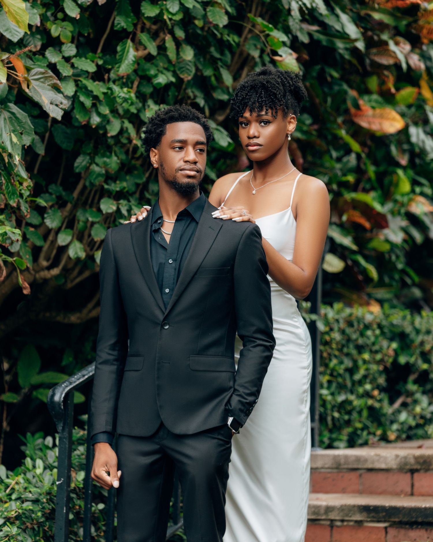 Couple in contrasting black and white attire pose against garden backdrop.