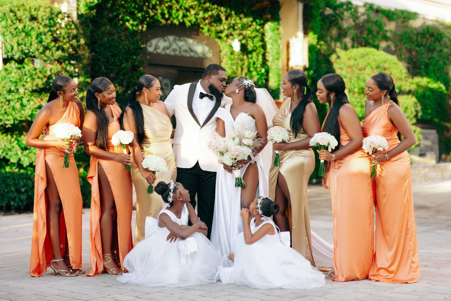 Wedding party poses in orange and white attire in a garden setting.
