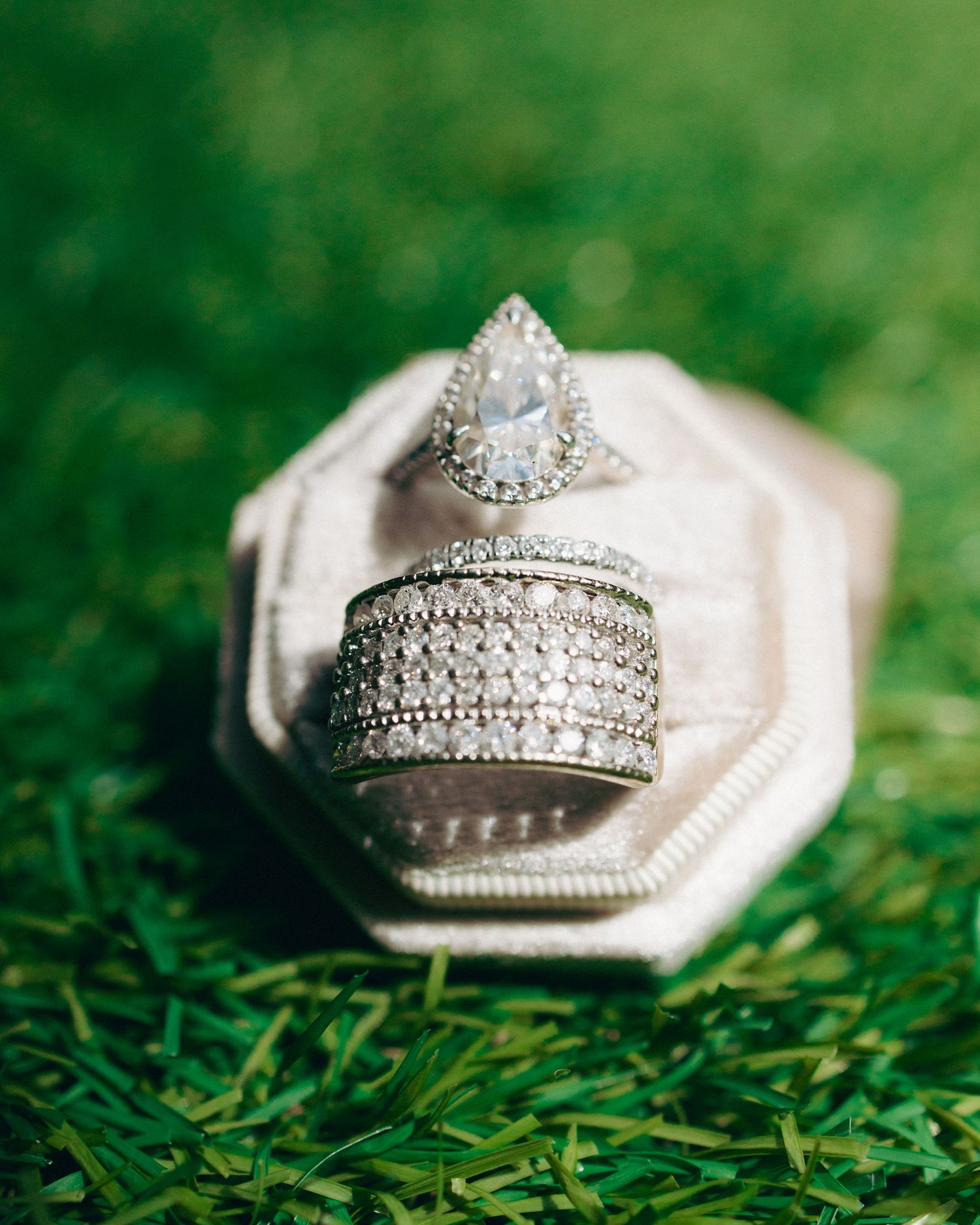 Wedding rings with intricate diamond details resting on lush green grass in a macro photography series.