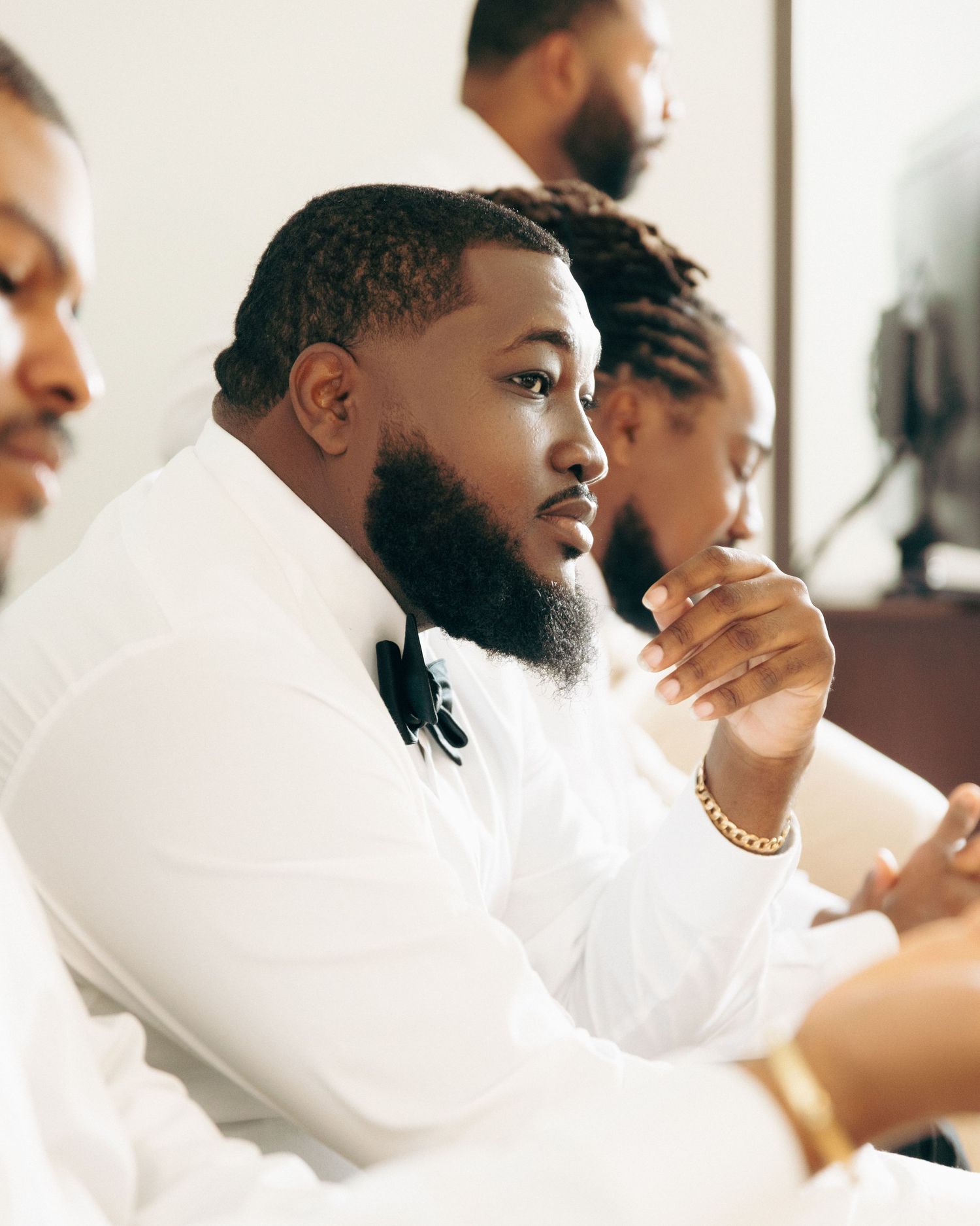 A person in white formal wear sits thoughtfully during wedding preparations.