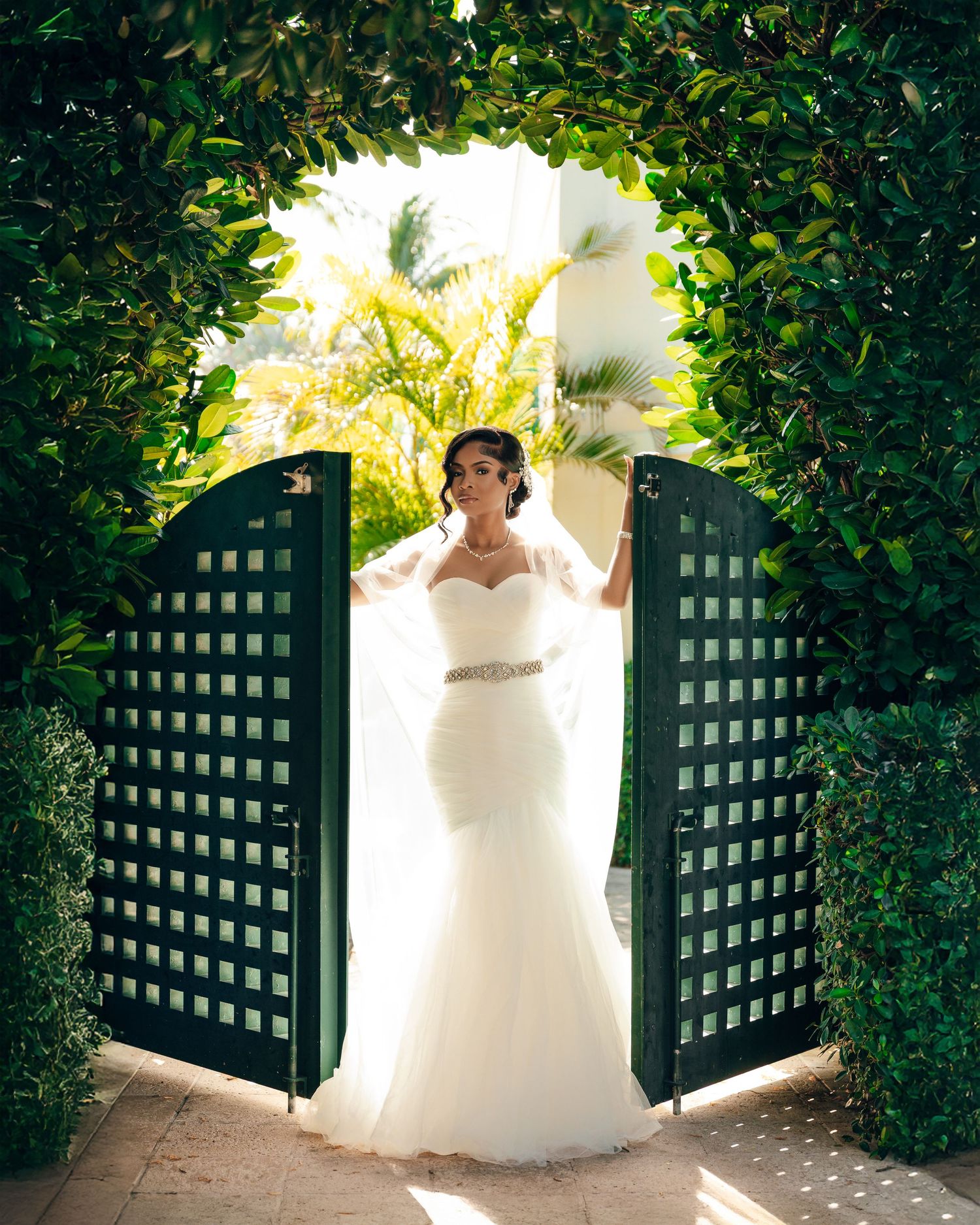A wedding dress photographed from different angles against a white wall and black lattice garden gate in natural lighting.