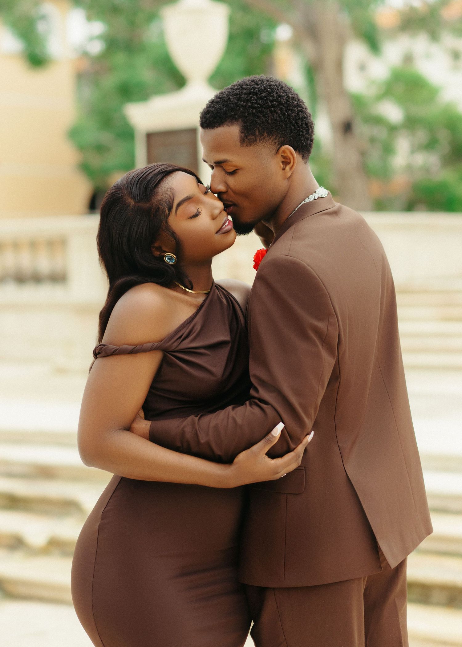 A romantic couple in brown outfits embrace intimately during an outdoor photo session.