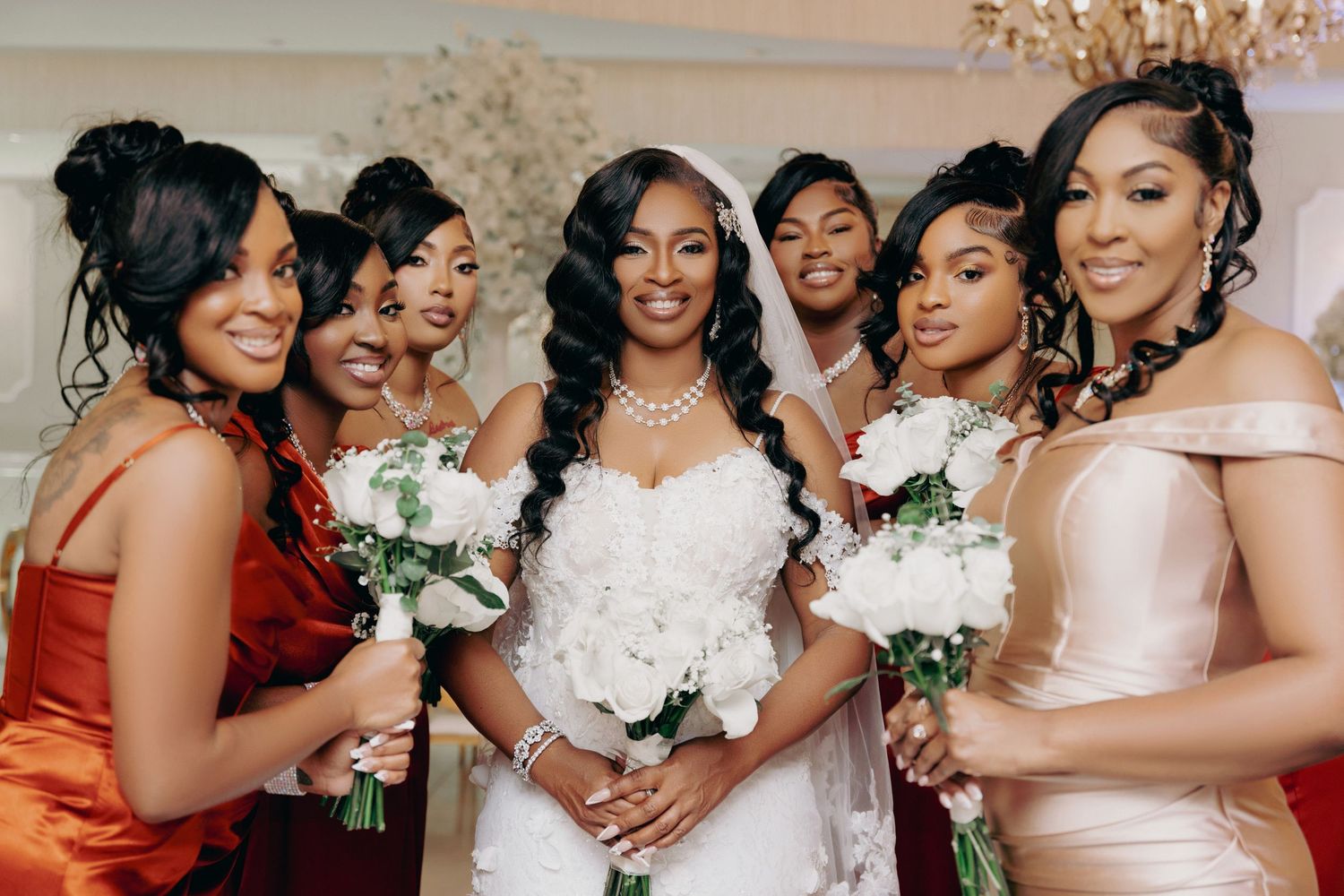 Bridesmaids in burgundy dresses hold white bouquets while celebrating at wedding.