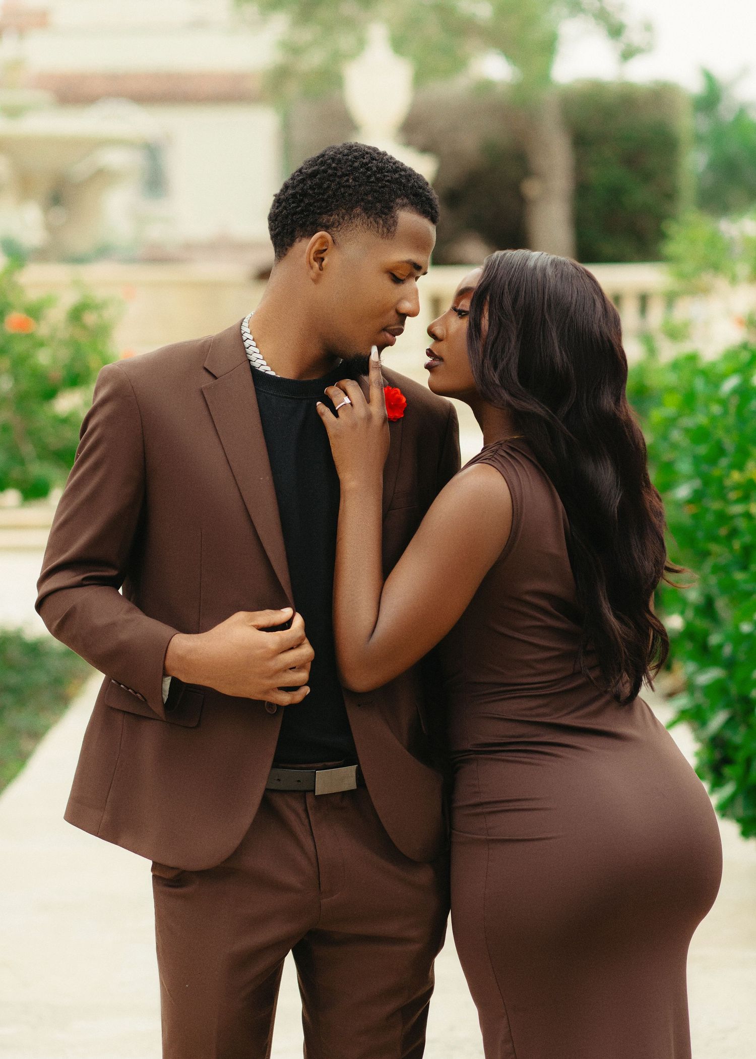 Couple shares intimate moments in coordinated brown formal wear during outdoor photography session.