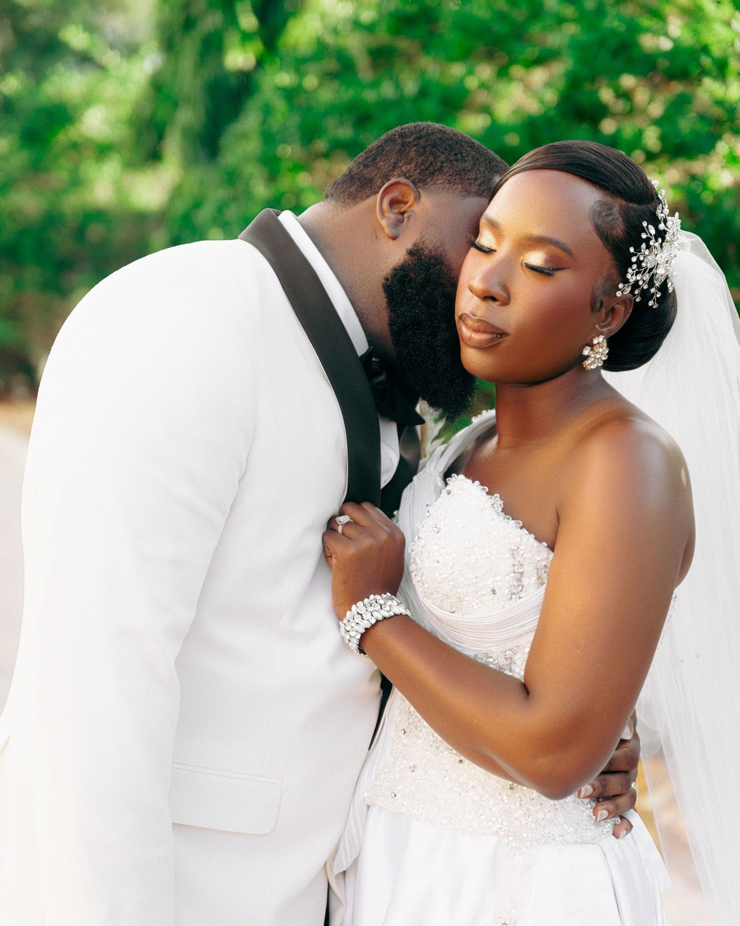 A romantic wedding portrait shows a couple embracing outdoors, with the bride in a white lace gown and delicate hair accessories.