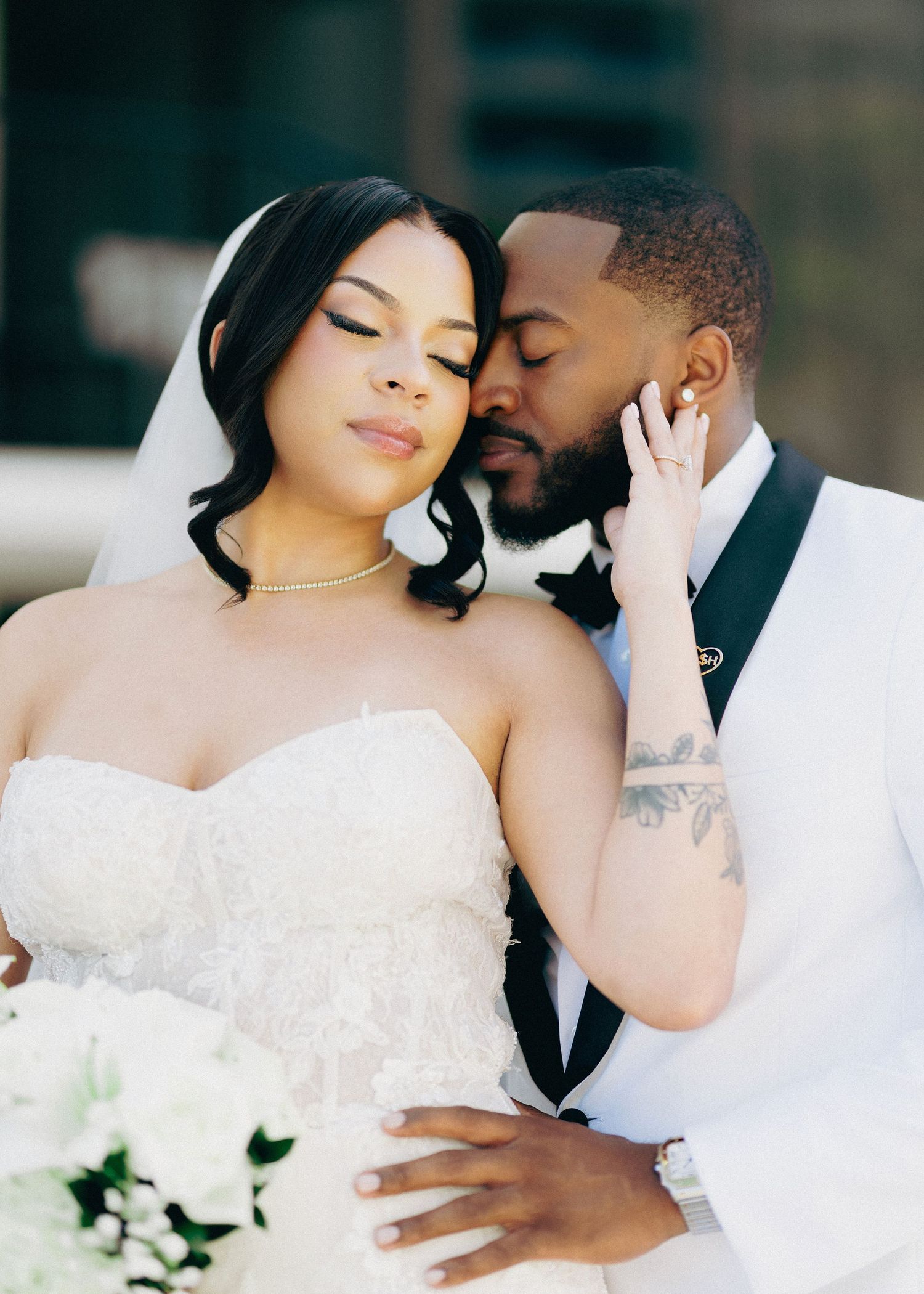 Bride and groom share an intimate moment in wedding attire, with the groom gently nuzzling the bride's cheek.