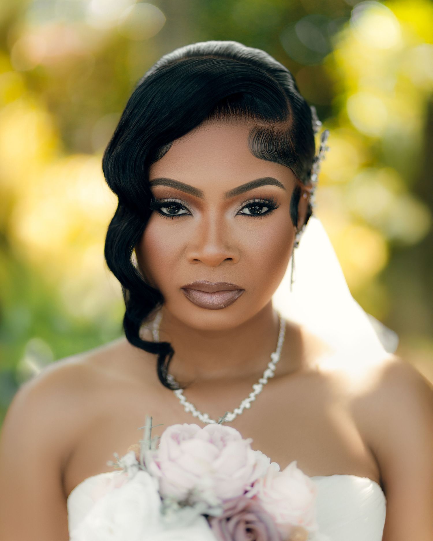 Elegant bridal portrait with pearl necklace and strapless white gown against soft bokeh background.