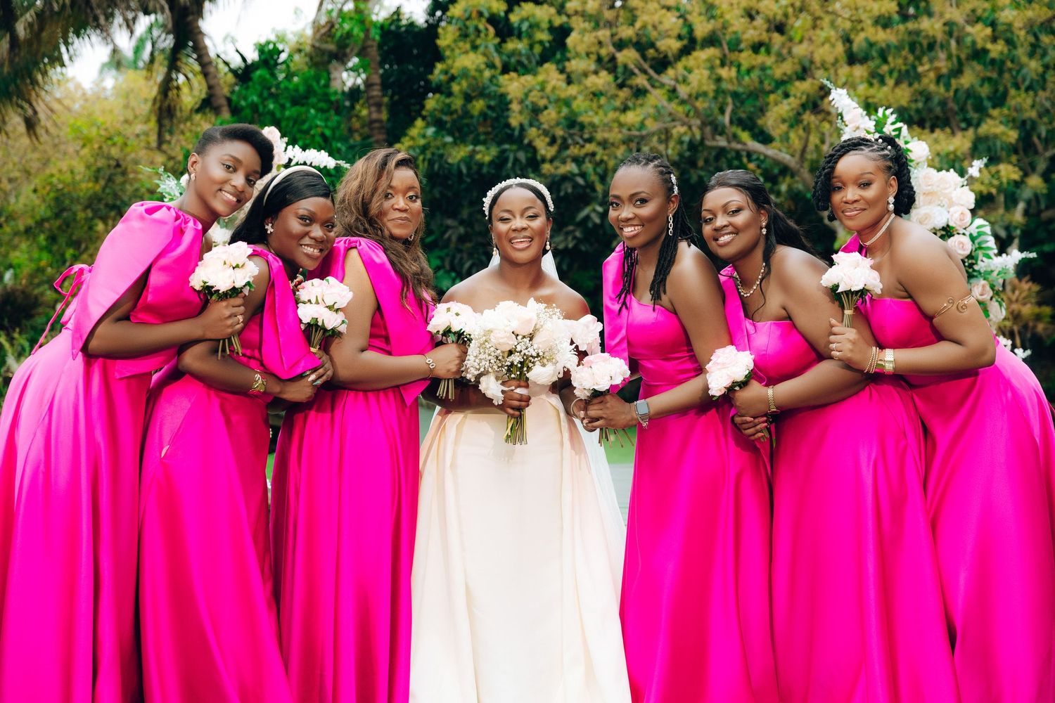 Wedding party in bright pink dresses poses joyfully on the lawn during an outdoor celebration.