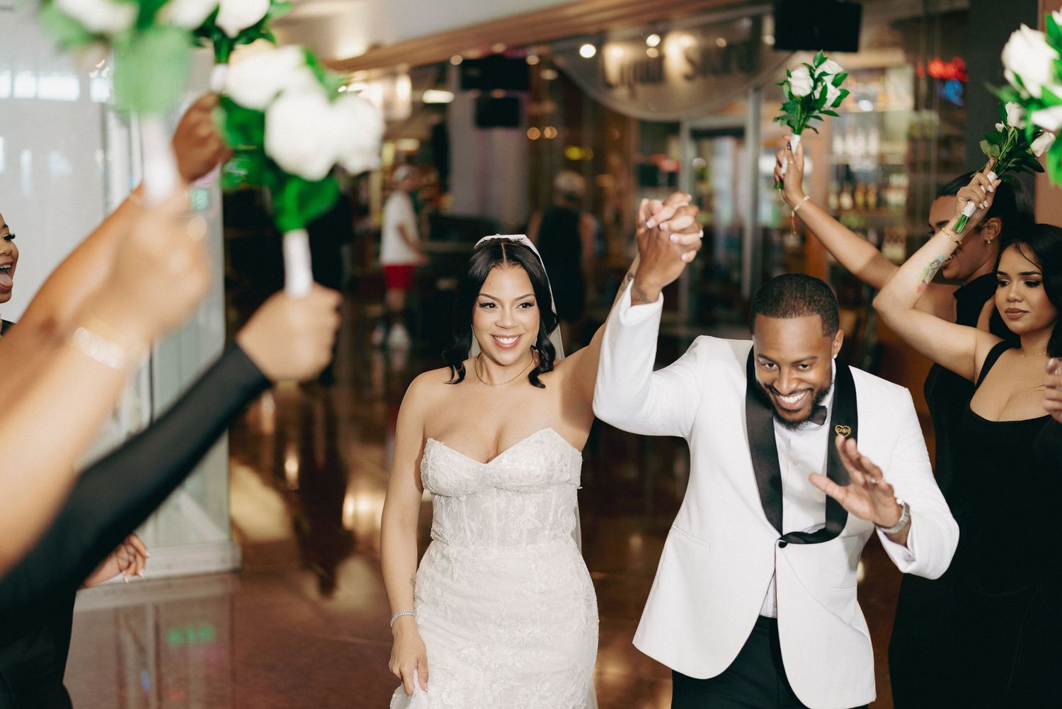 Smiling bride and groom make grand entrance as guests wave white roses in celebration.