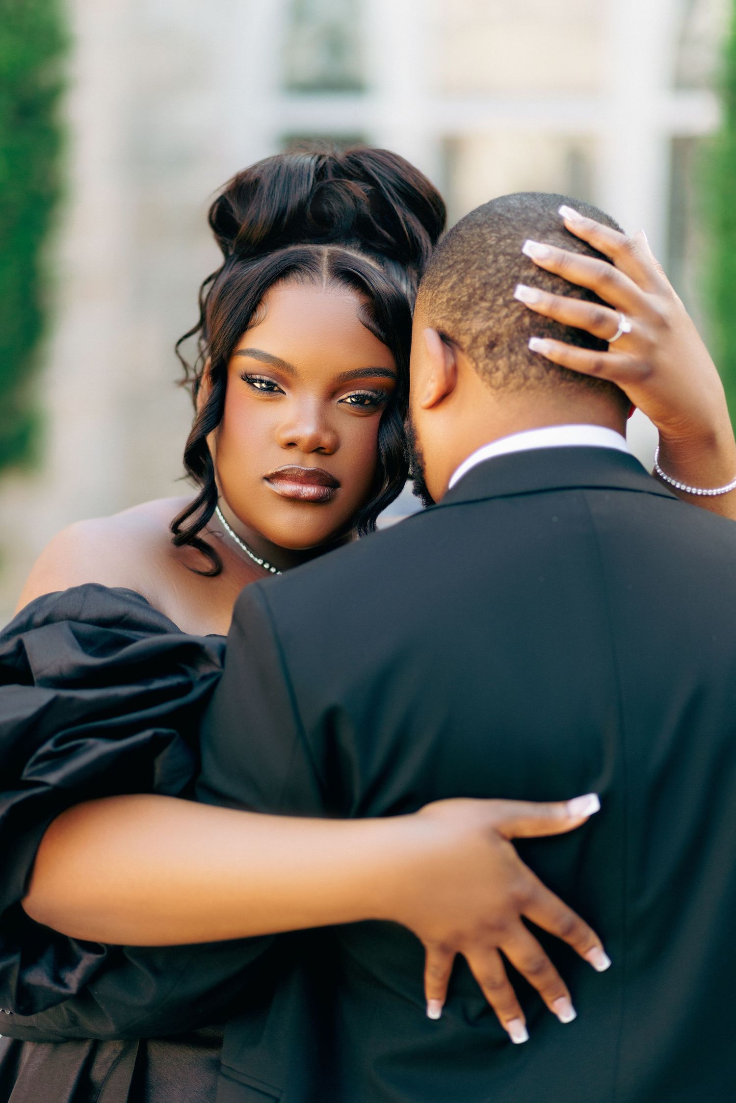 A romantic couple embraces during an outdoor portrait session, with the woman wearing an elegant black dress.