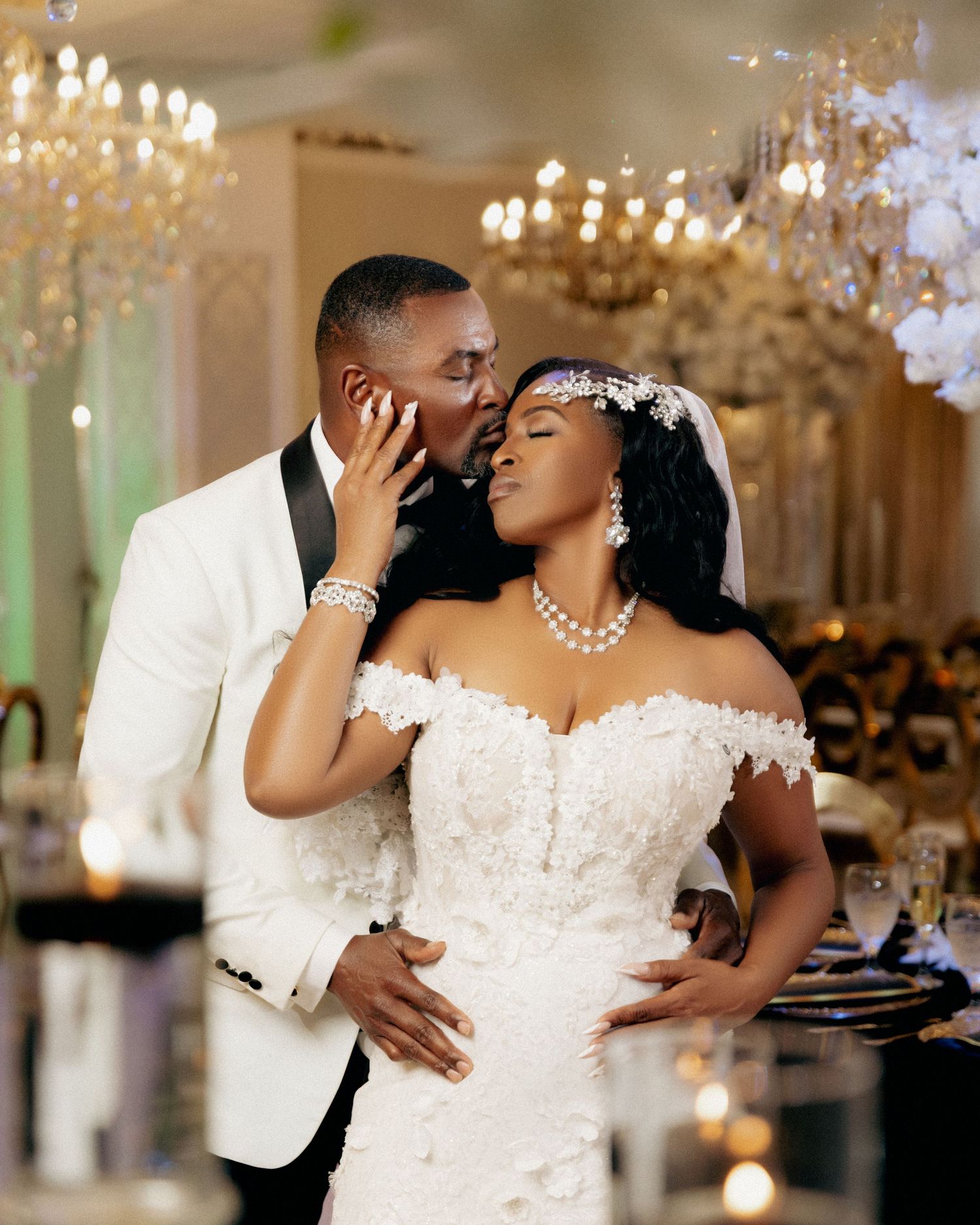 Elegant wedding couple shares intimate moments under crystal chandeliers in a luxurious ballroom setting.