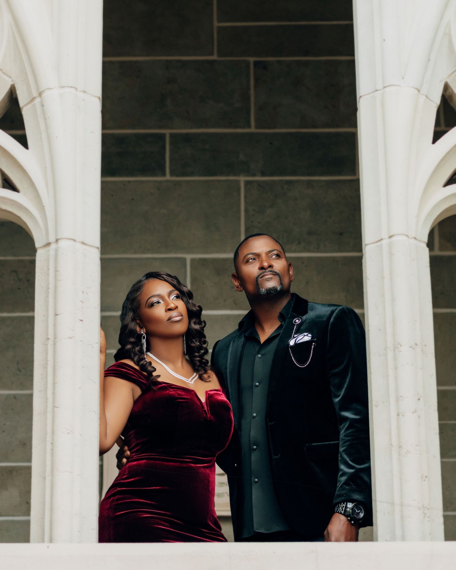 Couple in formal attire posing against architectural columns for engagement photos.