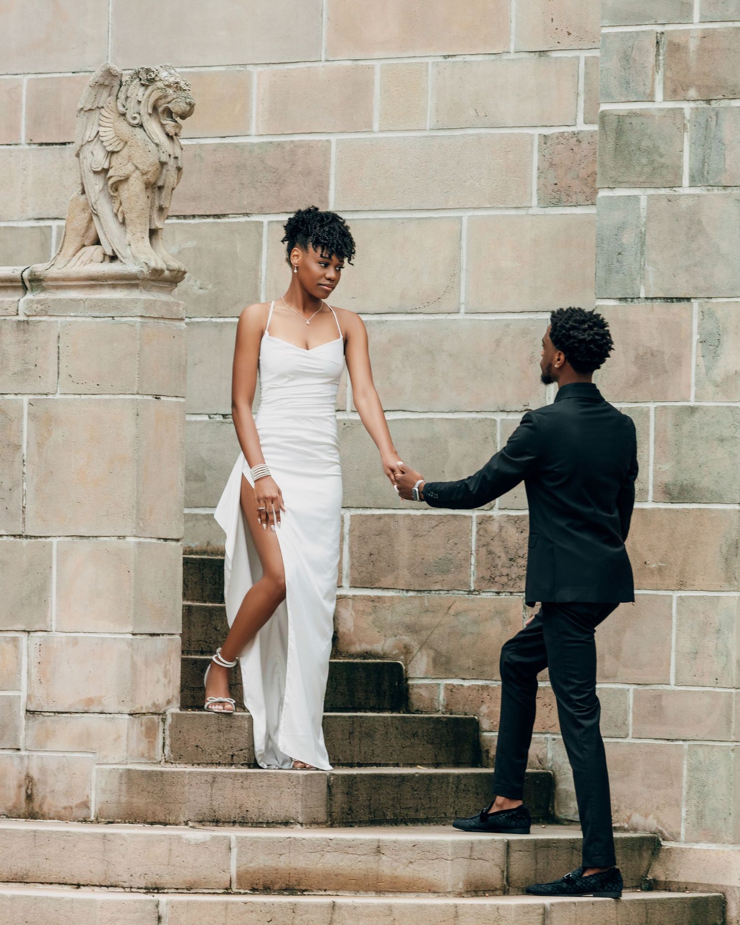 Couple ascending stone steps together in formal attire.