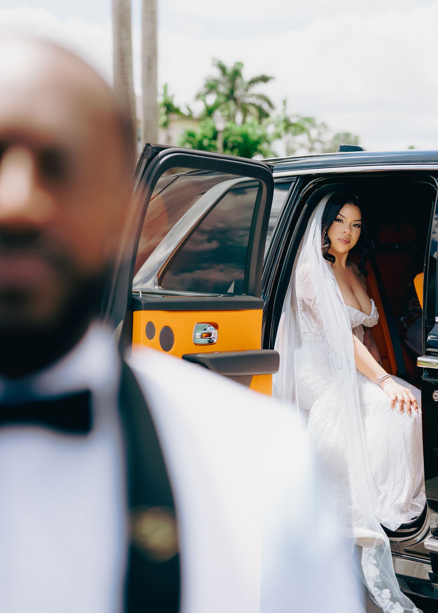 Bride in white gown and veil stepping out of a yellow and black vehicle on her wedding day.