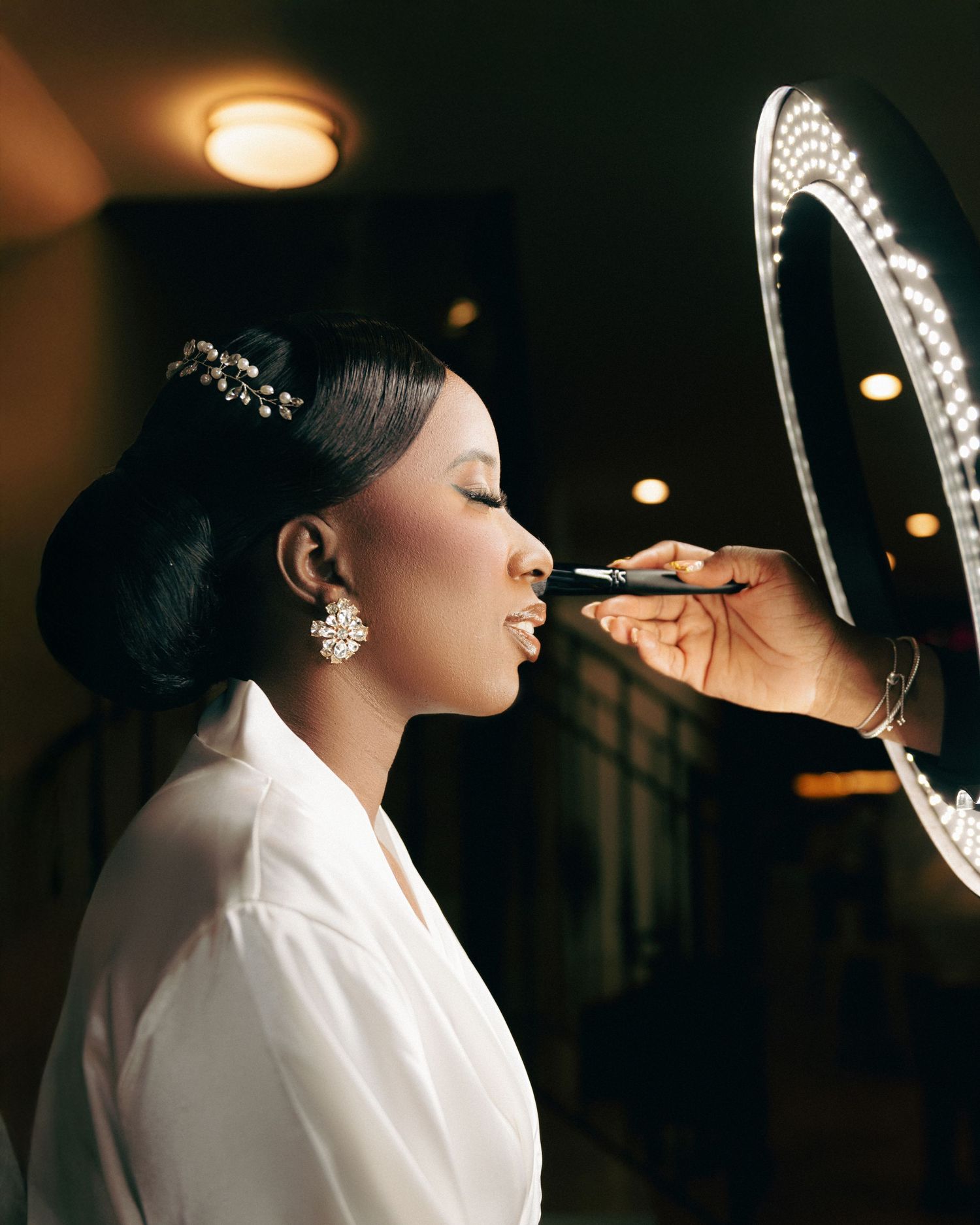 A makeup artist applies cosmetics using a lighted mirror in an elegant setting.
