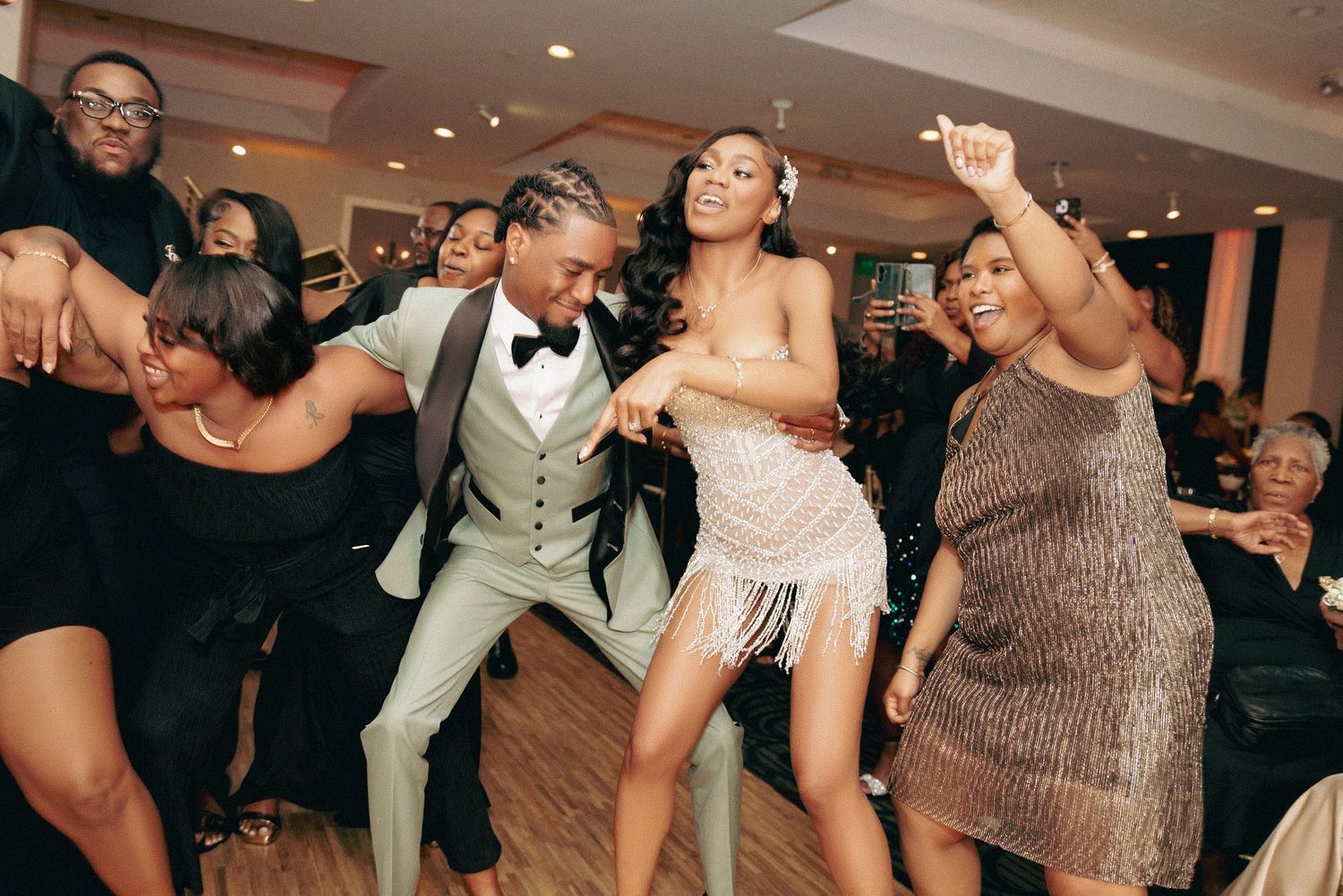 Wedding guests dance energetically on the dance floor at a reception, showing off their moves in formal attire.