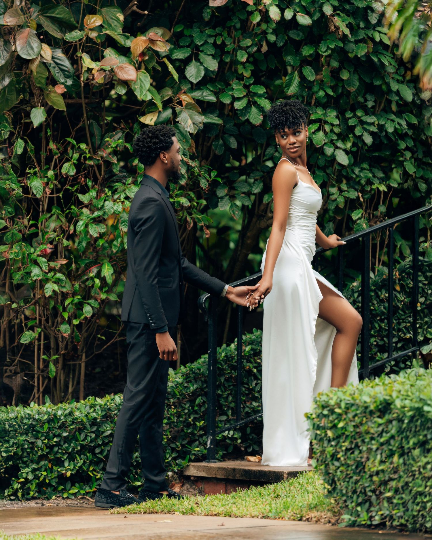 Couple shares intimate moments in garden setting with lush greenery.