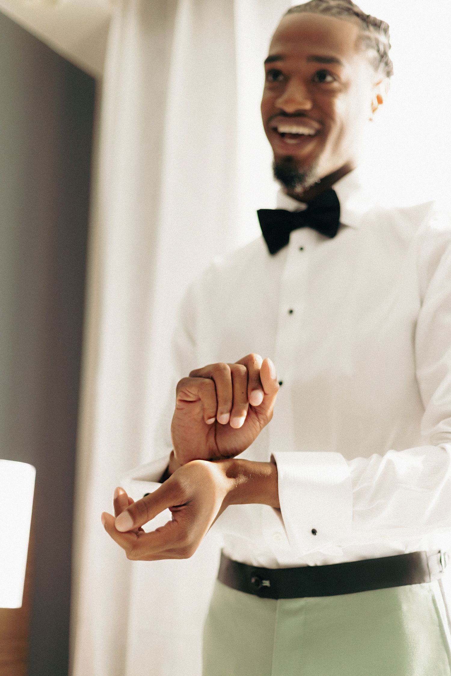 Close-up view of hands buttoning up a crisp white dress shirt against a light background.
