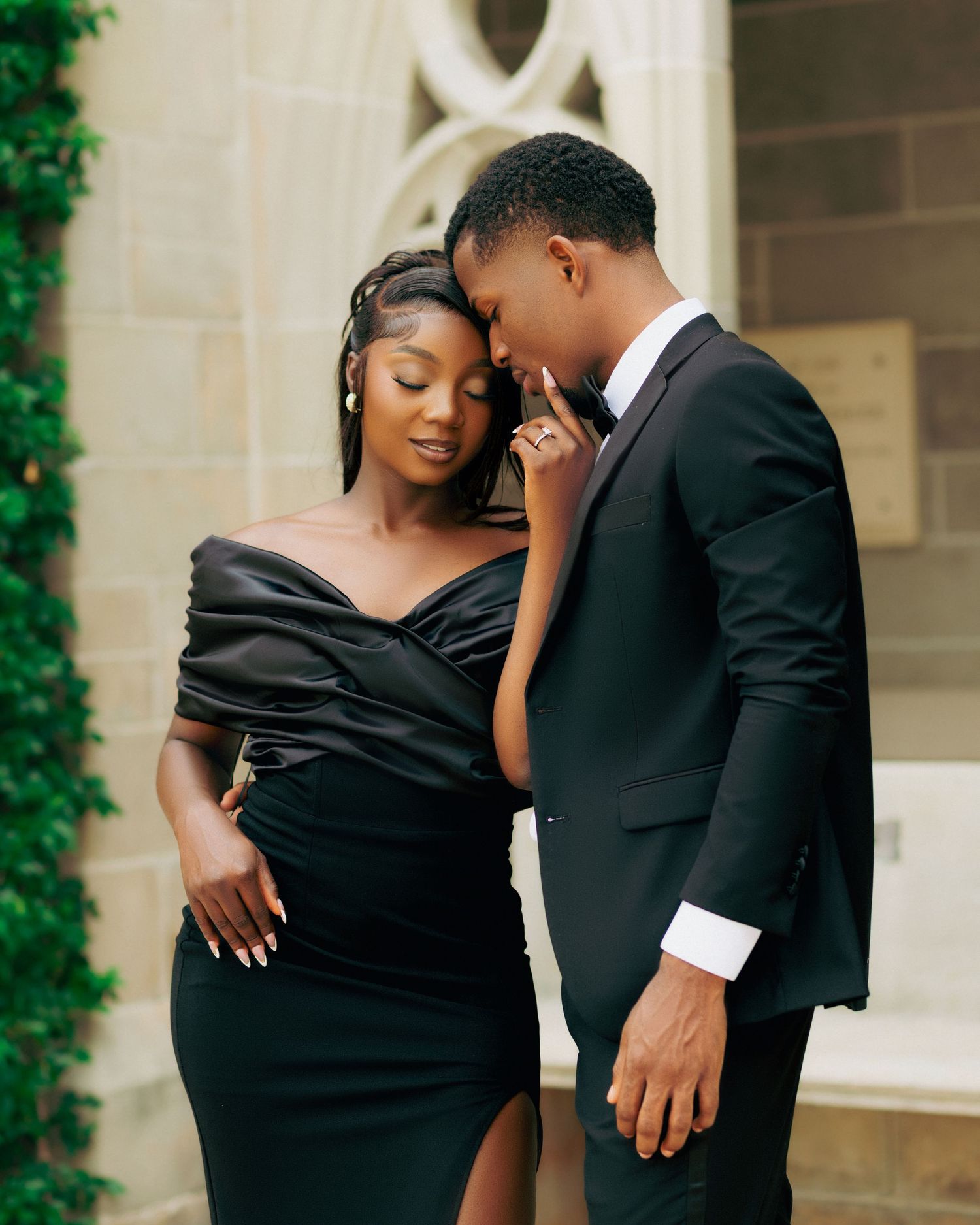 Romantic couple in formal black attire sharing intimate moments against stone wall.