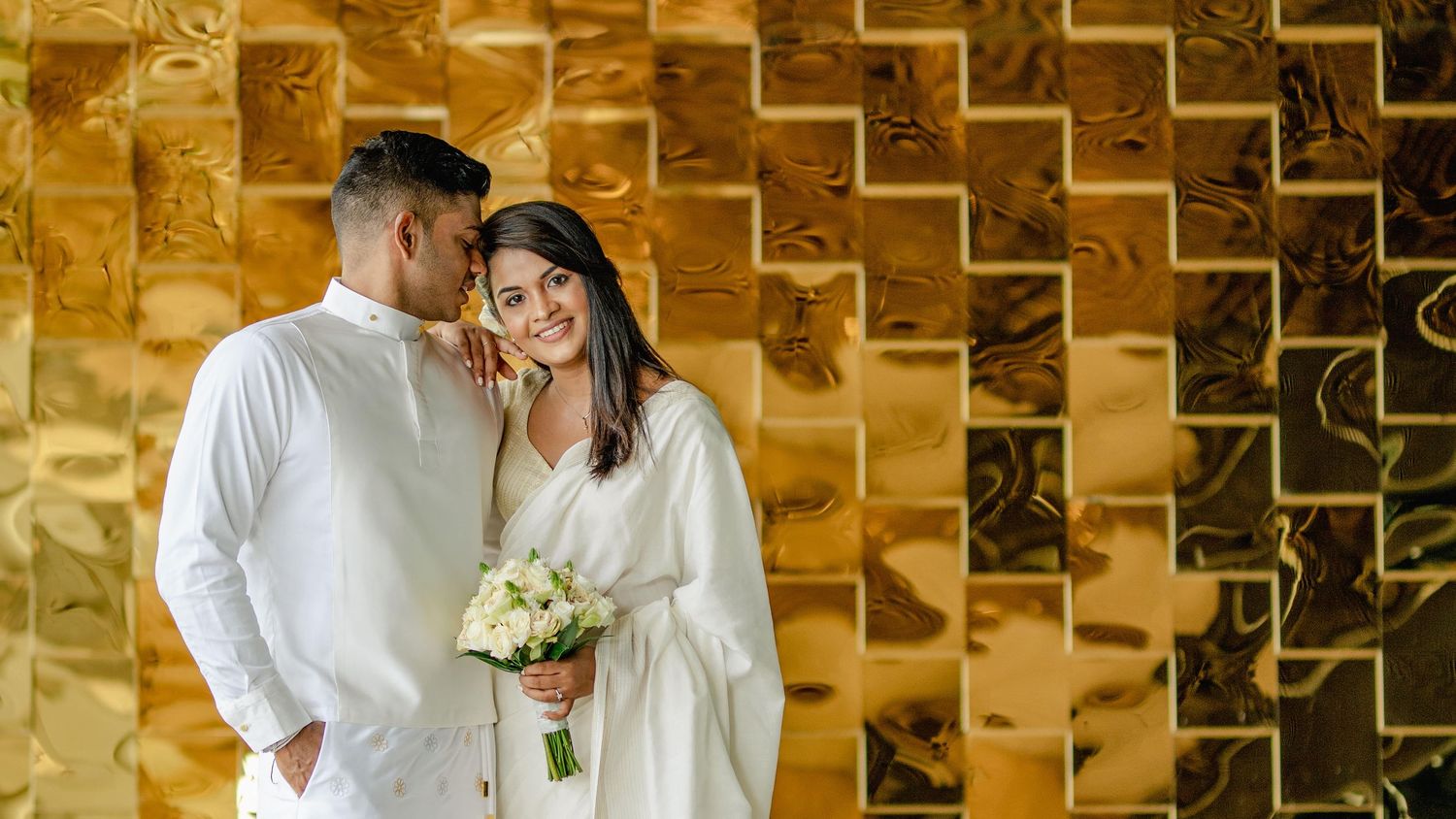 A romantic couple in white attire shares tender moments in a golden-tiled hallway during their wedding celebration.