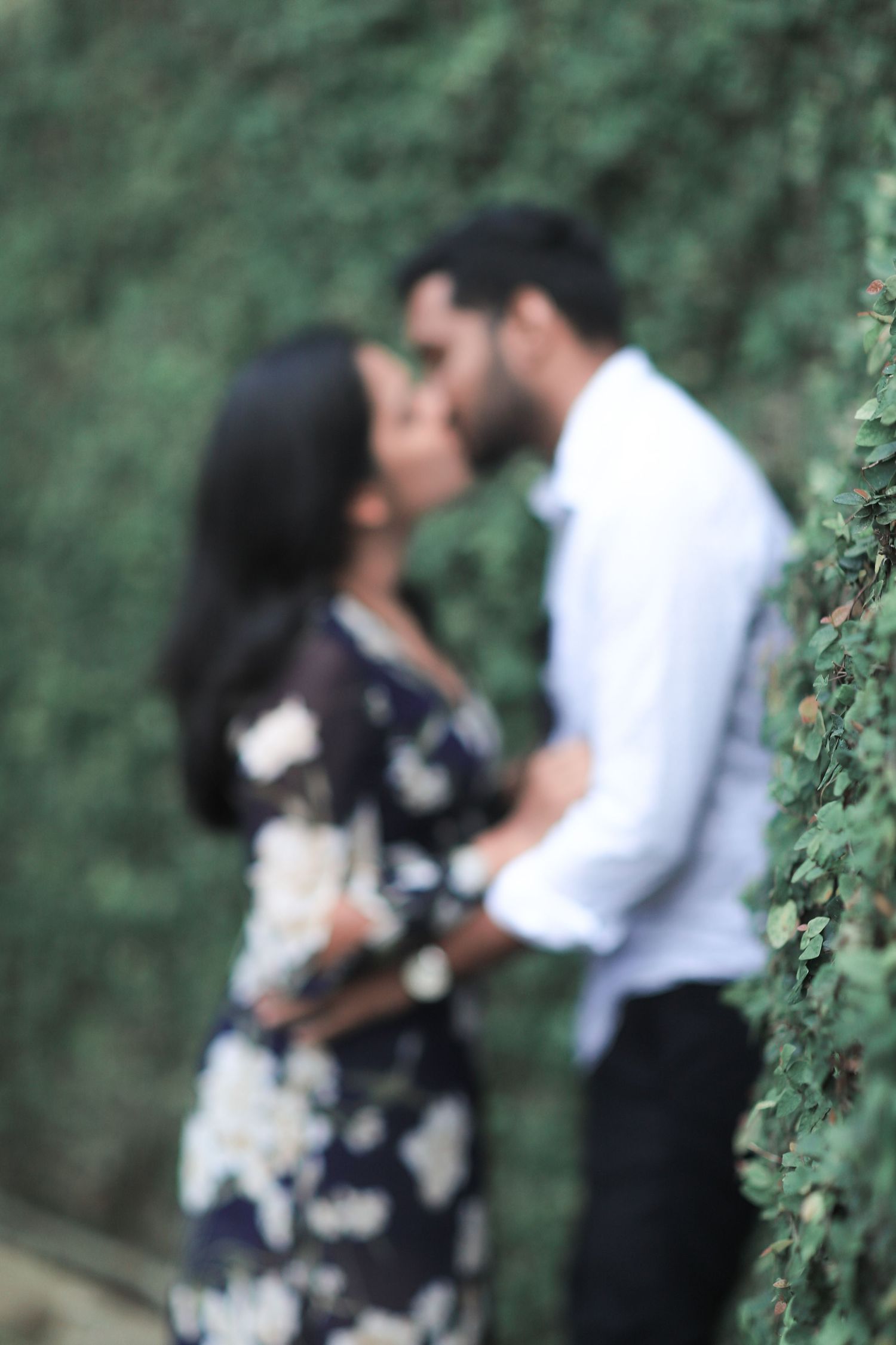 A romantic couple sharing an intimate moment in a garden setting with soft blurred focus and greenery in the background.