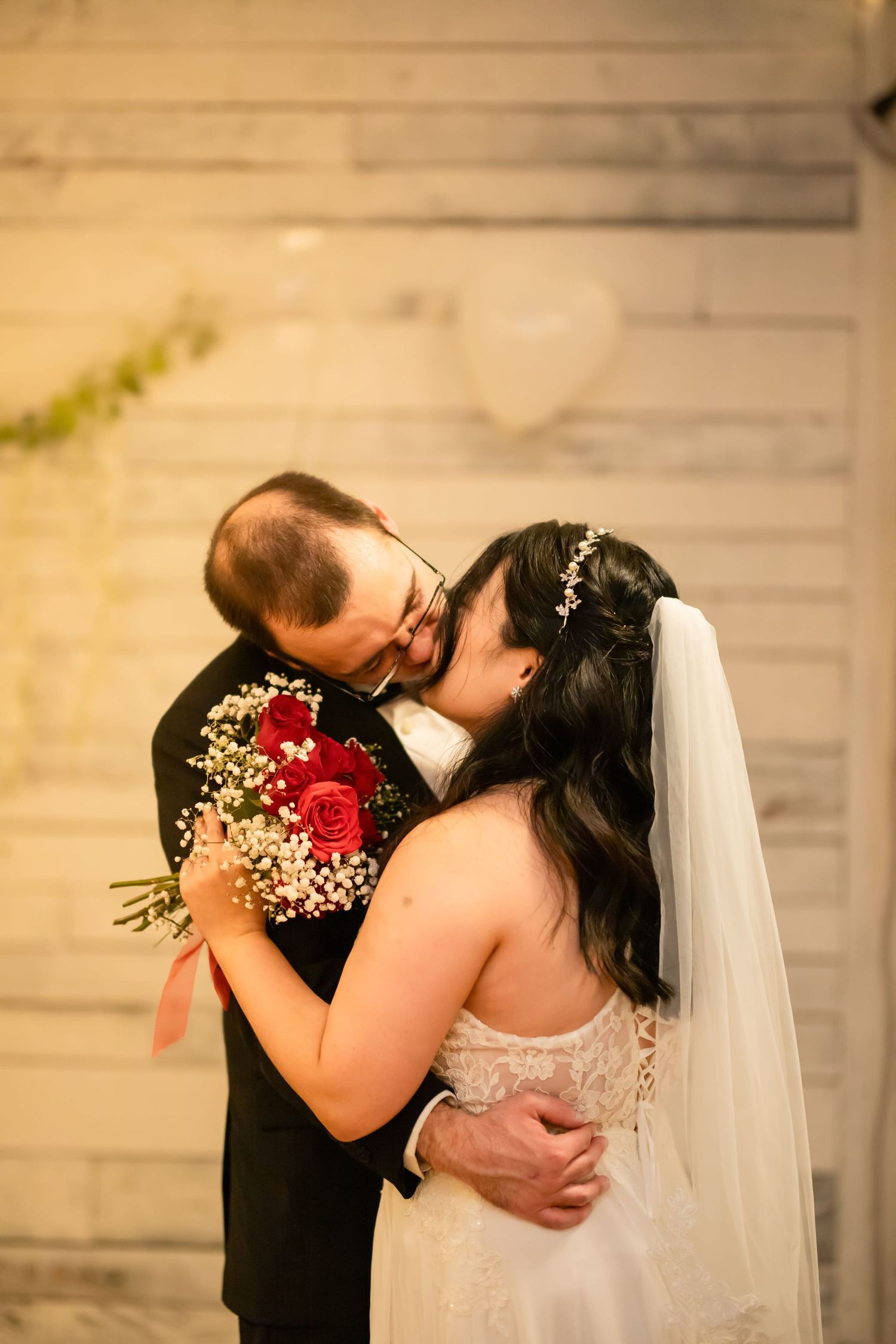 Couple embraces during their wedding ceremony with red roses and baby's breath bouquet.