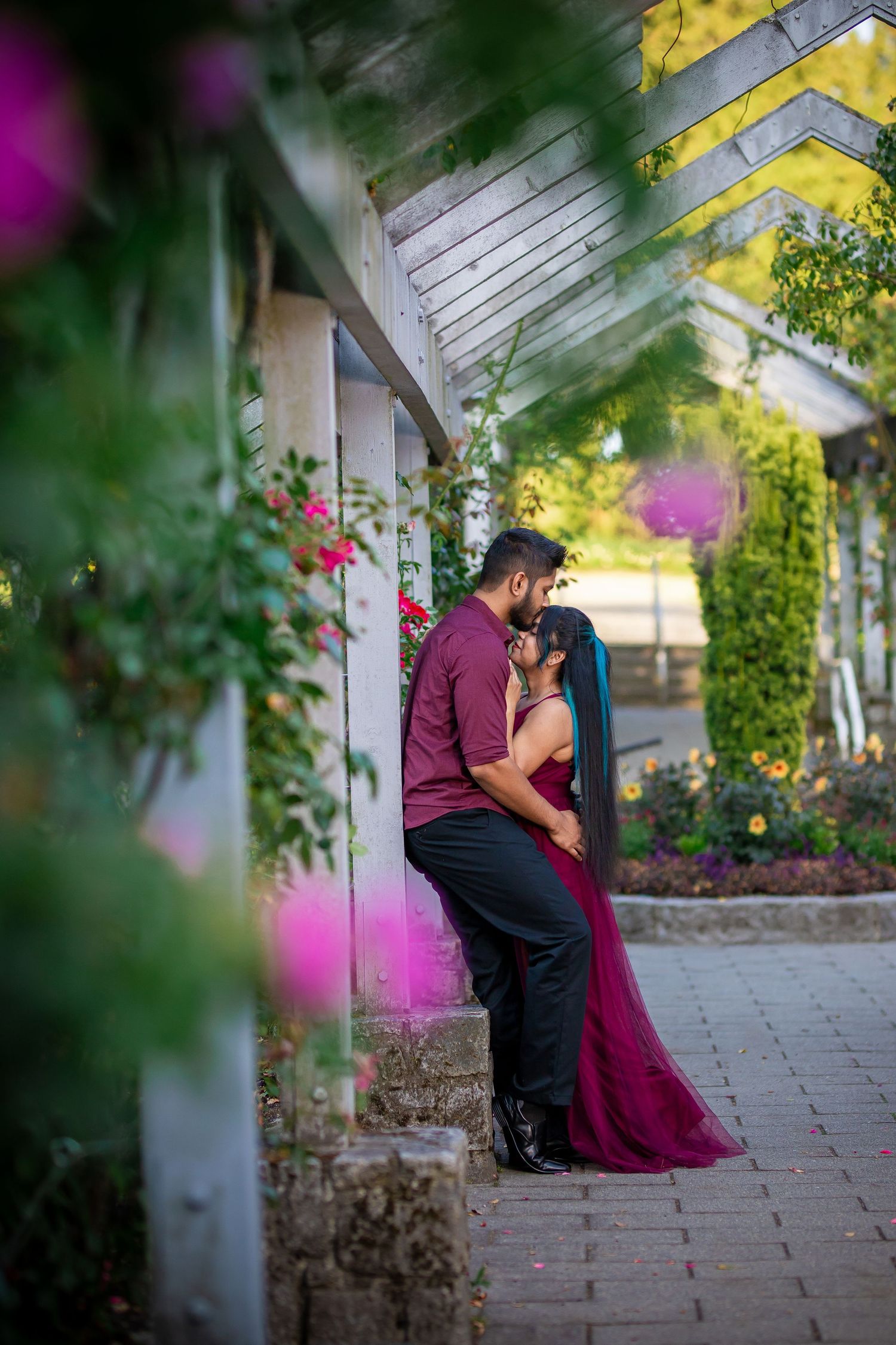 A romantic couple embraces in a garden setting with pink flowers and white columns creating a dreamy atmosphere.