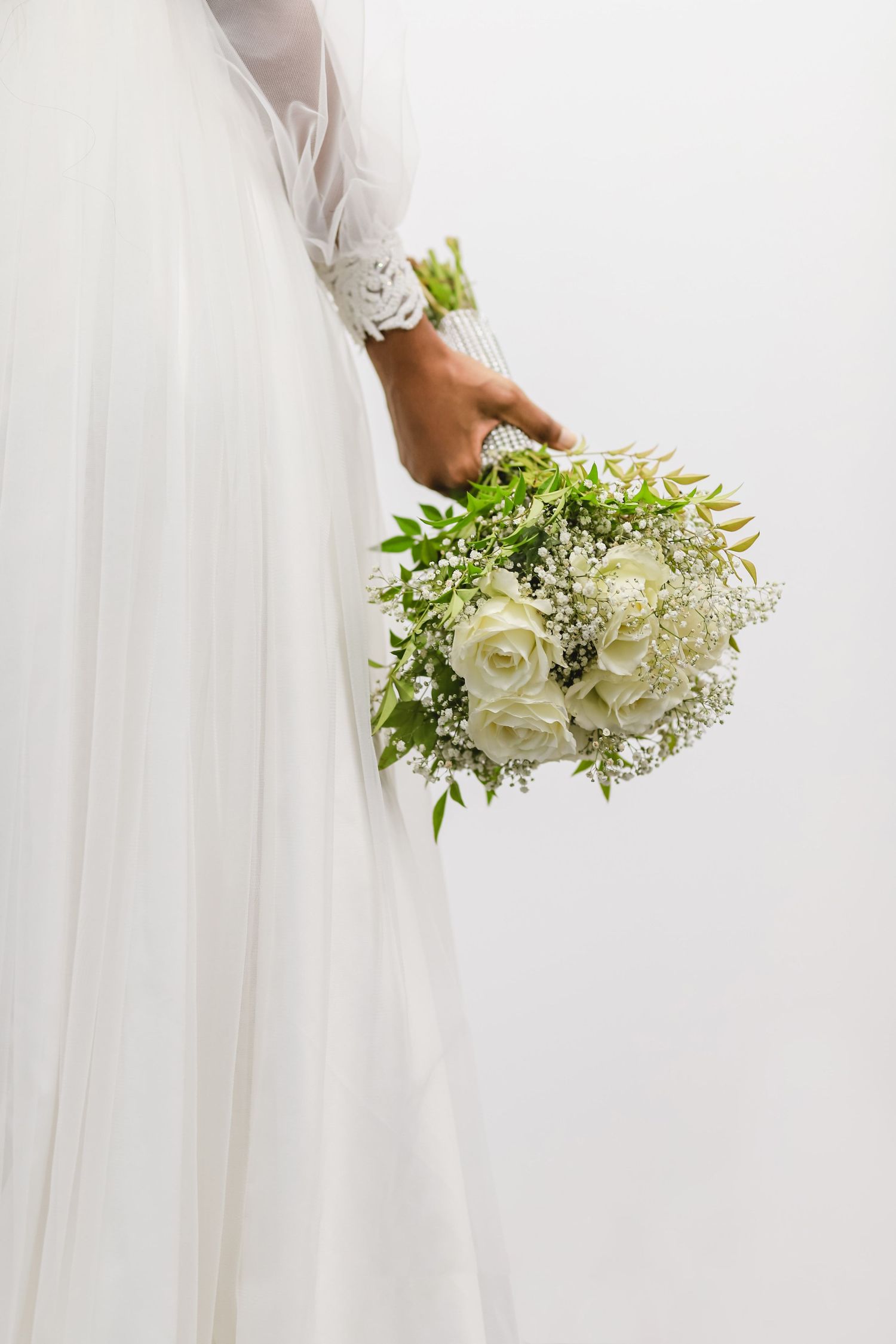Elegant white bridal bouquet with delicate flowers and greenery against a light background.