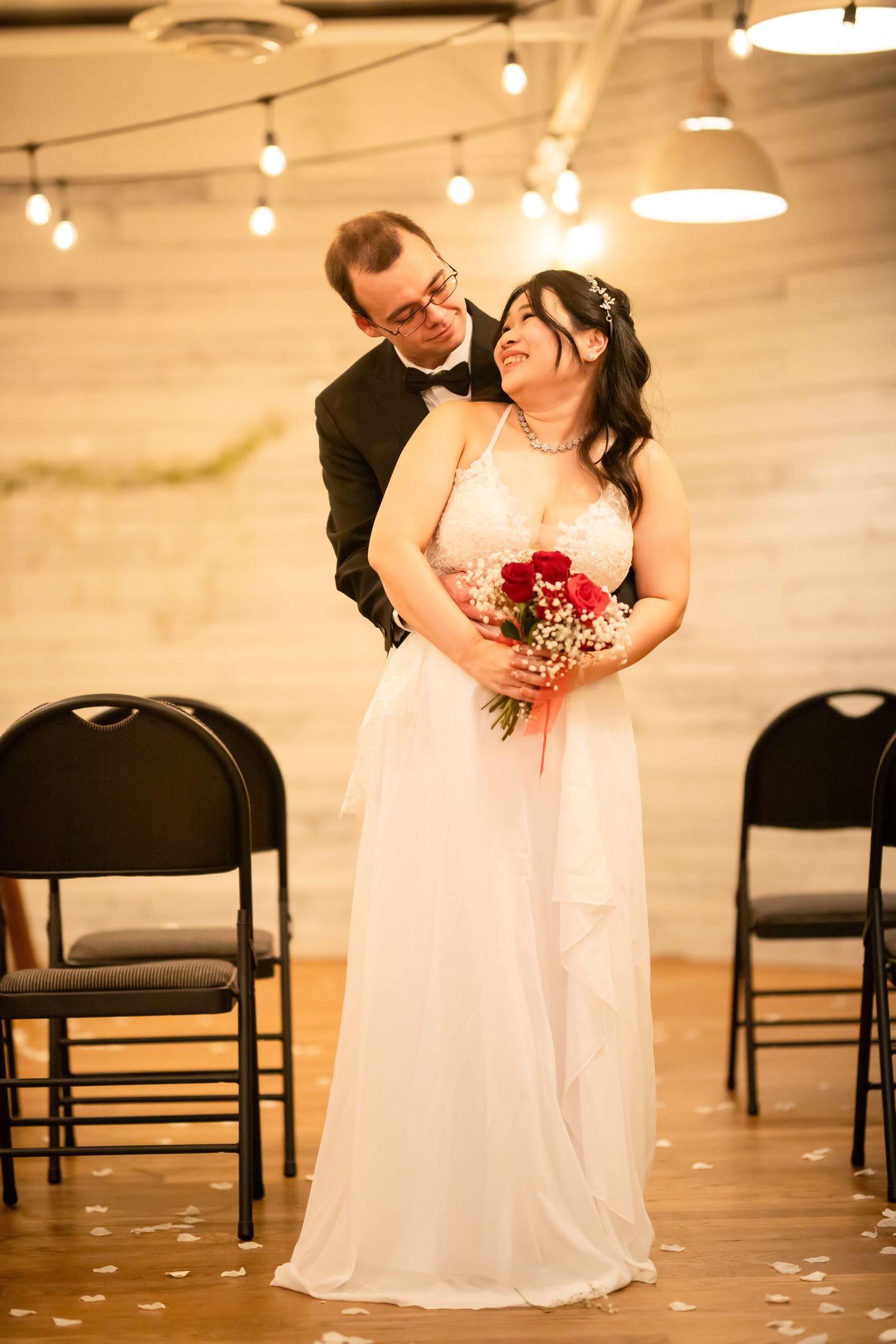Wedding couple shares tender moments among scattered rose petals and folding chairs.