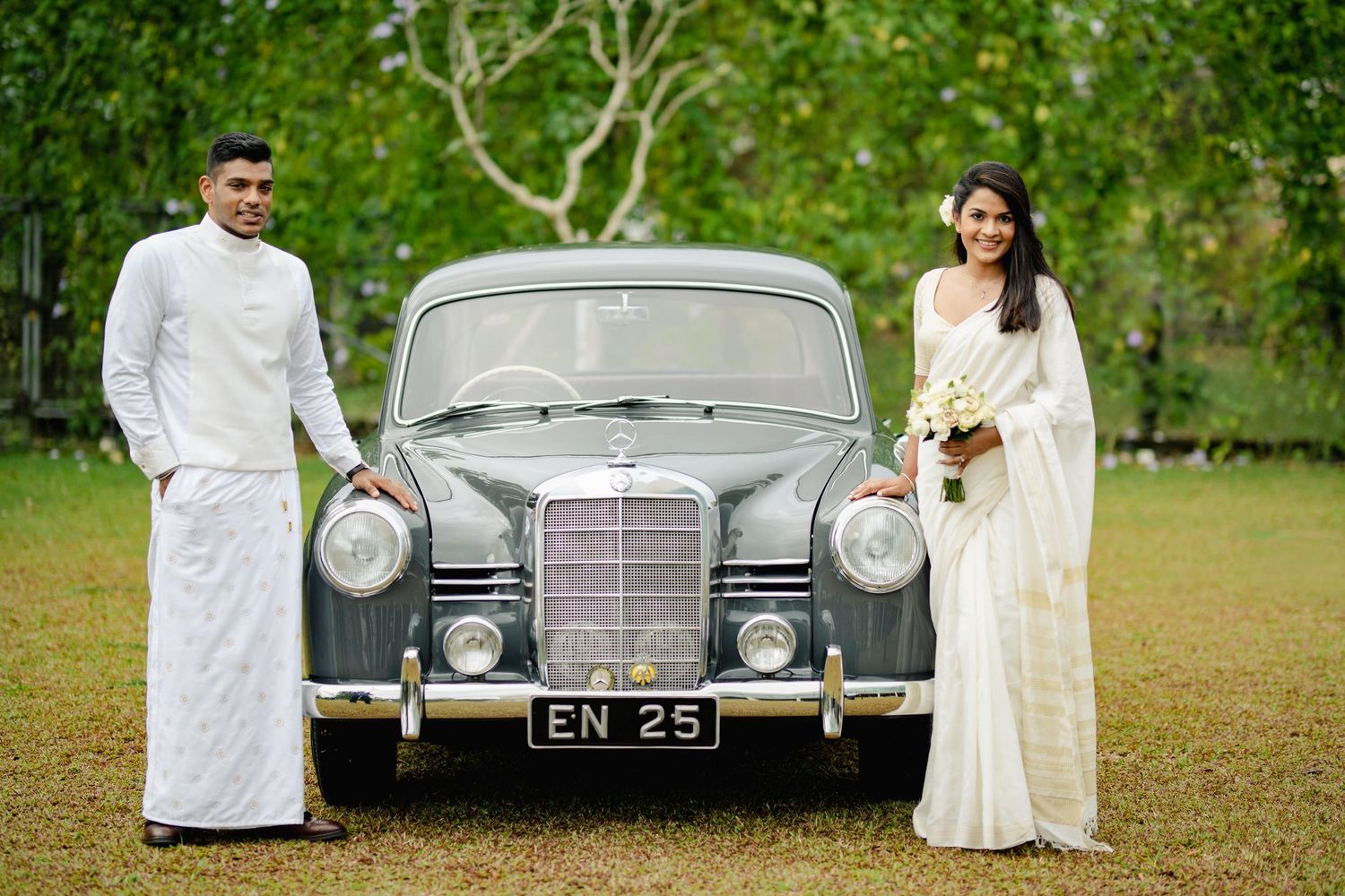 A vintage silver Mercedes-Benz classic car parked in a lush green garden setting during a special occasion.