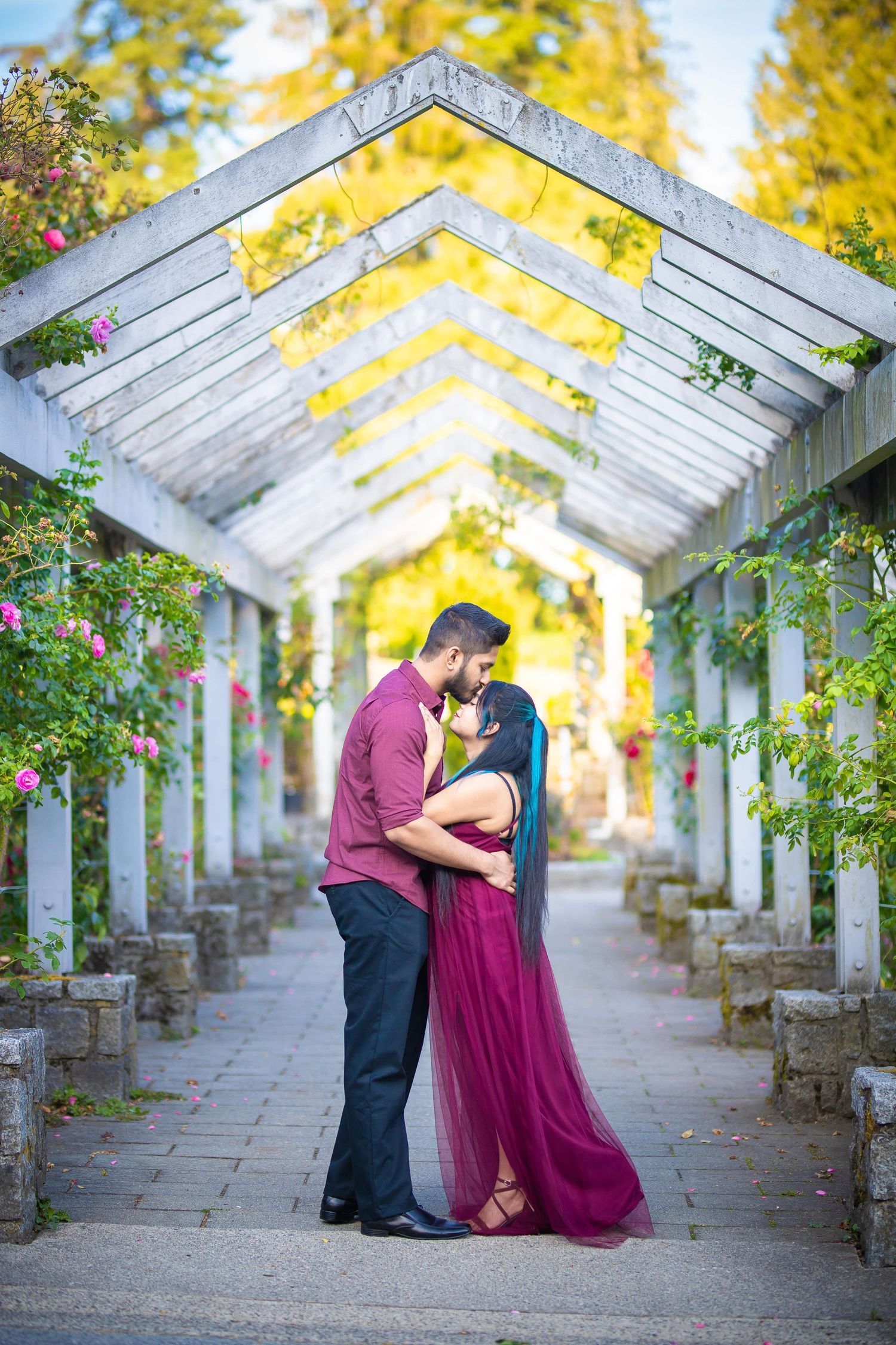 Romantic couple shares tender moments in a garden pergola with autumn foliage and golden light creating a dreamy atmosphere.