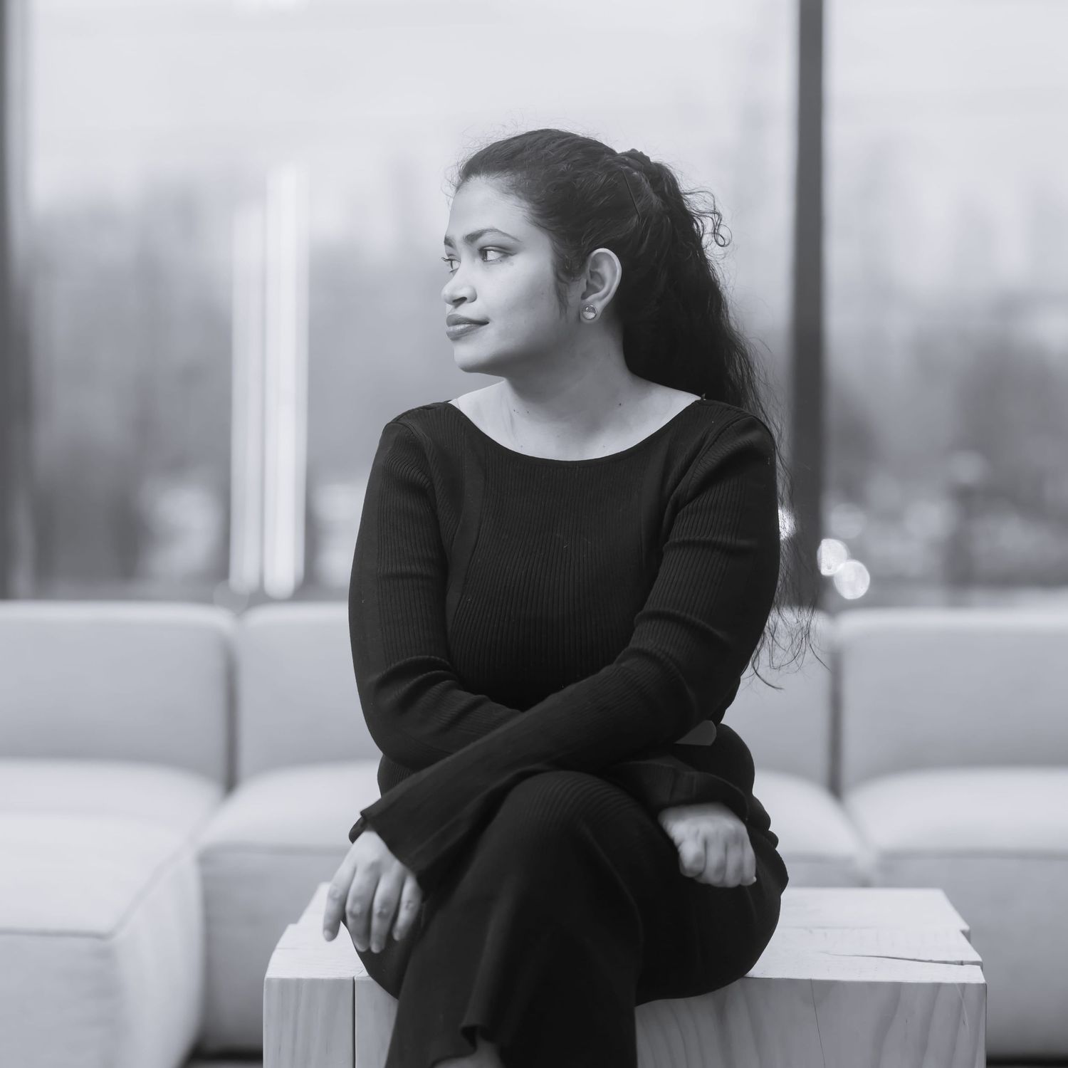 Black and white portrait series showing a woman in dark clothing sitting and posing on a white couch.