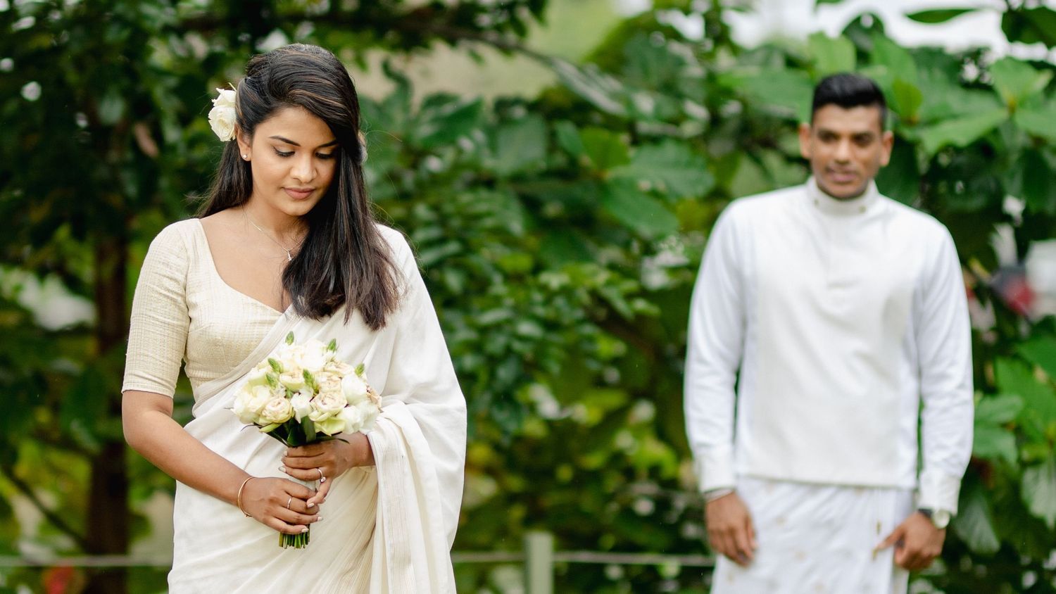 A wedding couple walks through a lush garden path surrounded by greenery during their outdoor celebration.