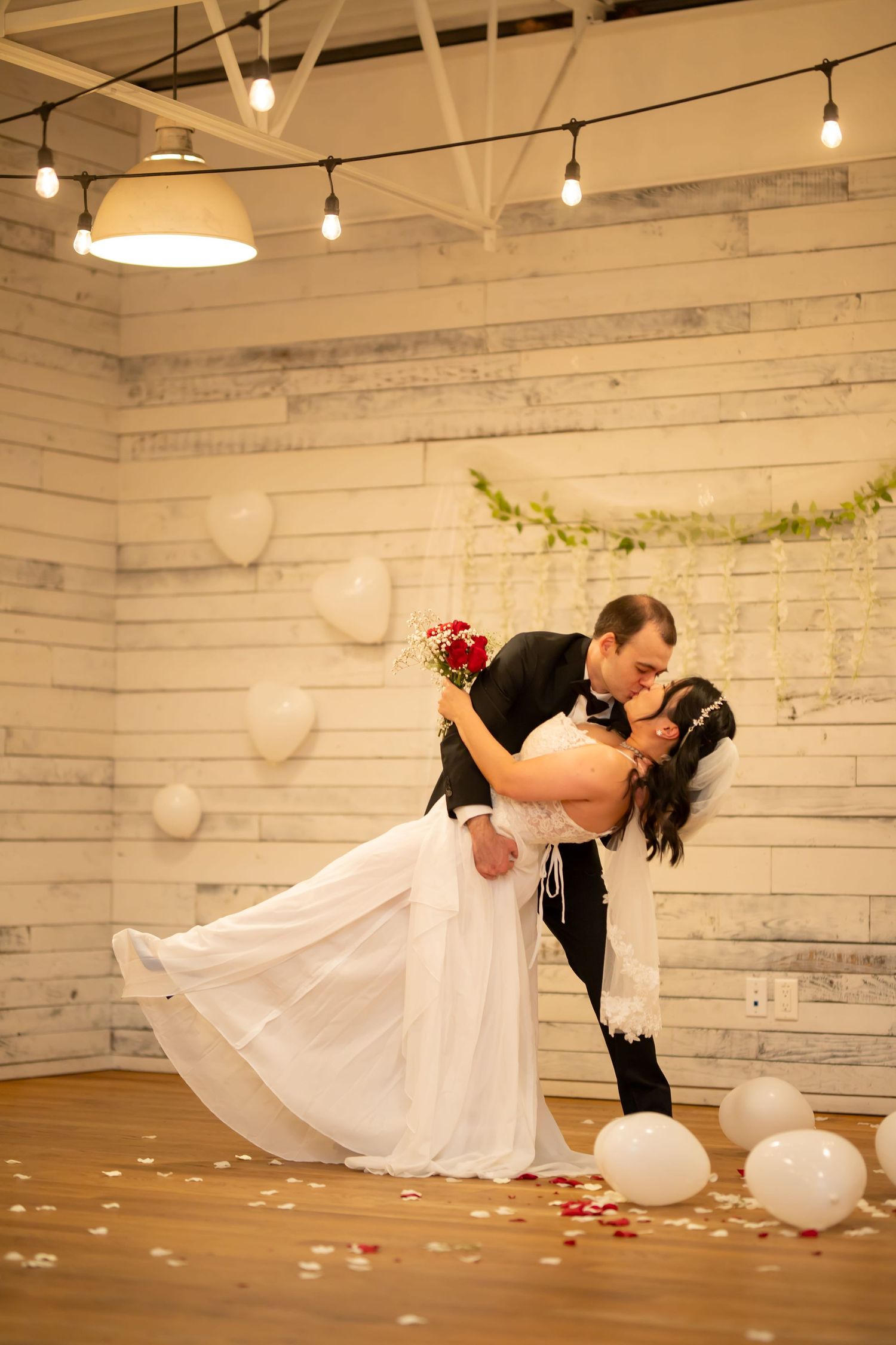 Romantic dip kiss sequence during wedding dance with string lights and white decor.