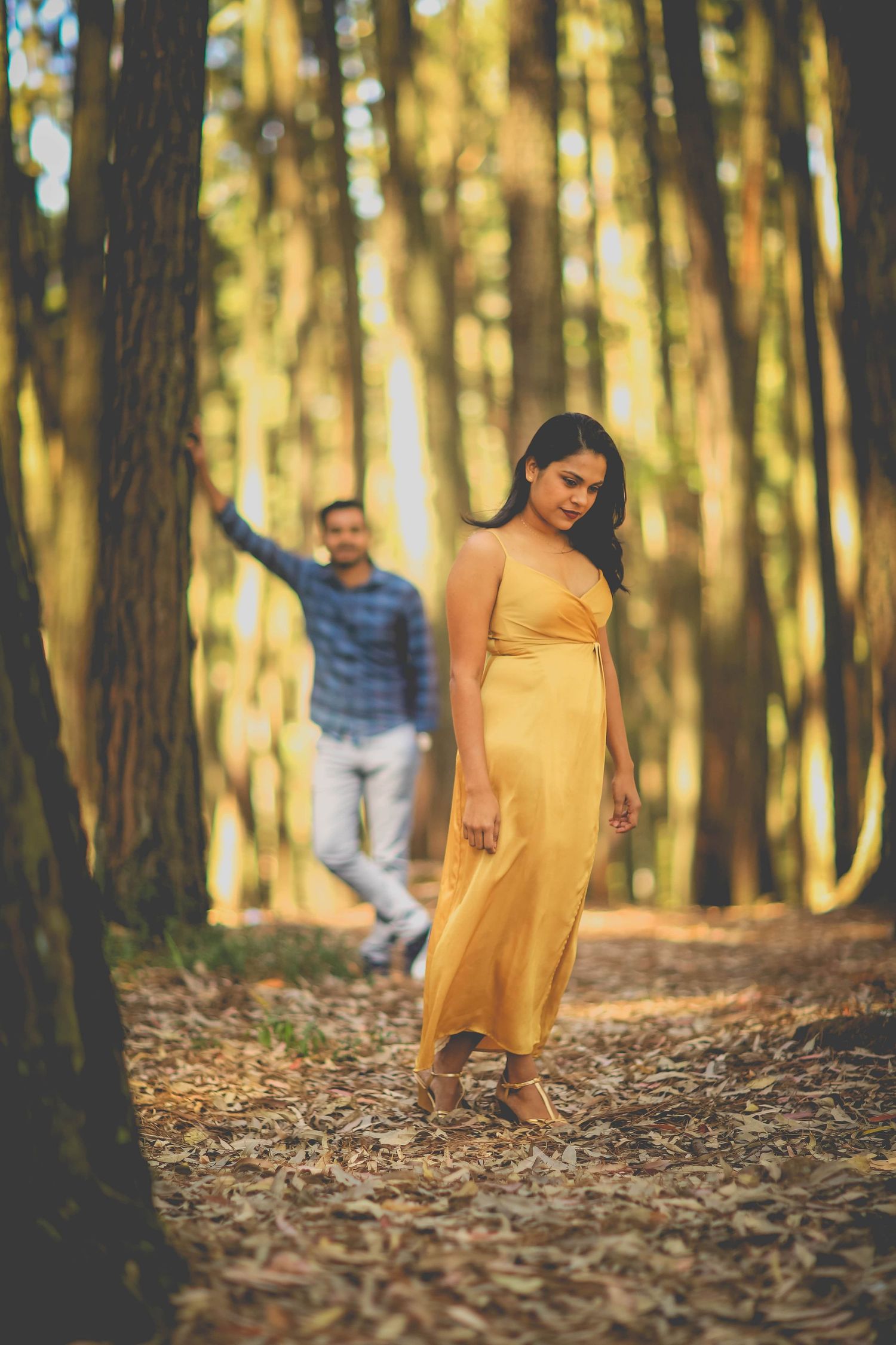 Artistic portrait of couple in forest with woman in yellow dress in foreground.