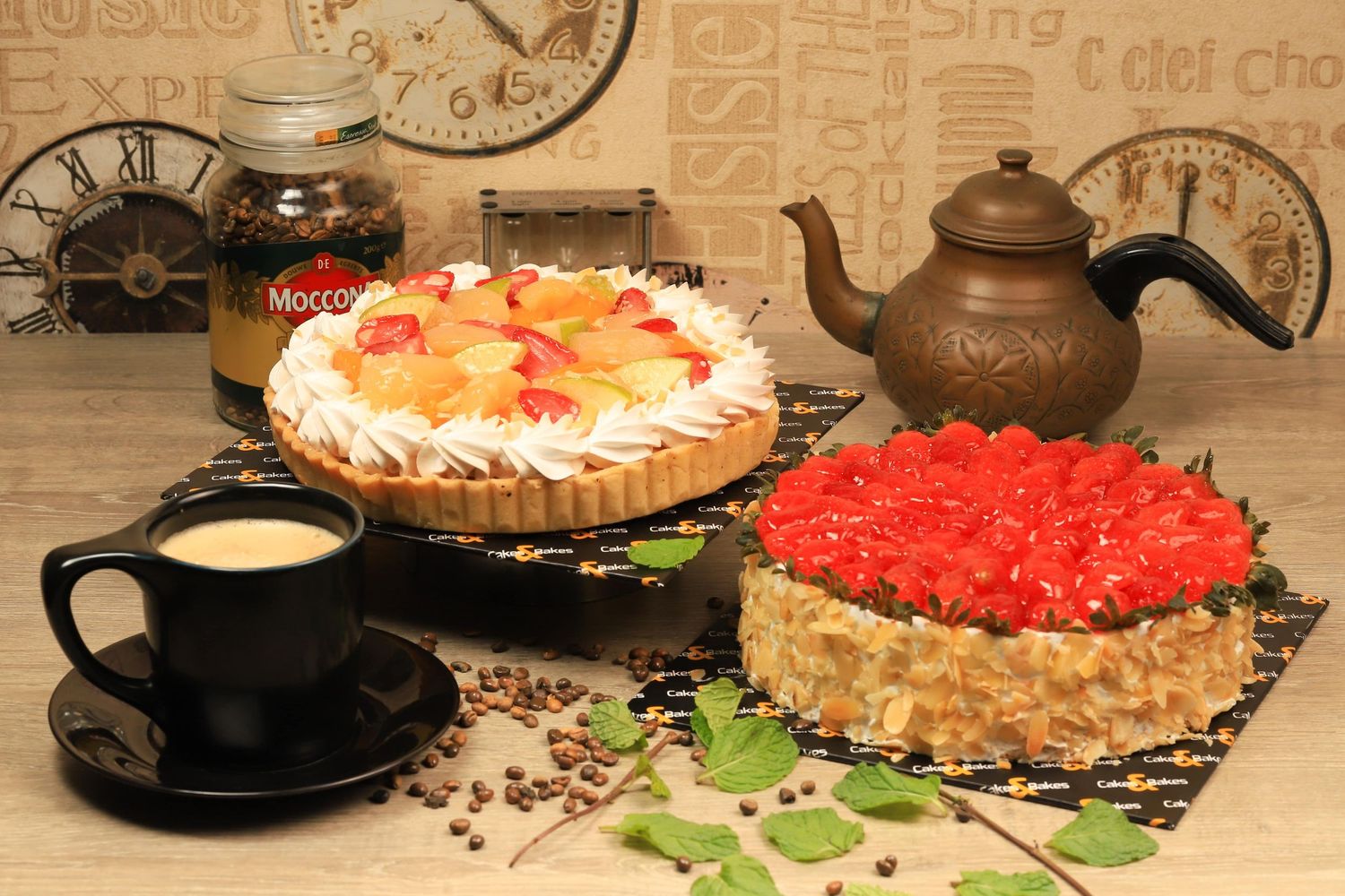 Assortment of elegant cakes, pastries and desserts displayed with coffee and tea service on a rustic wooden table.
