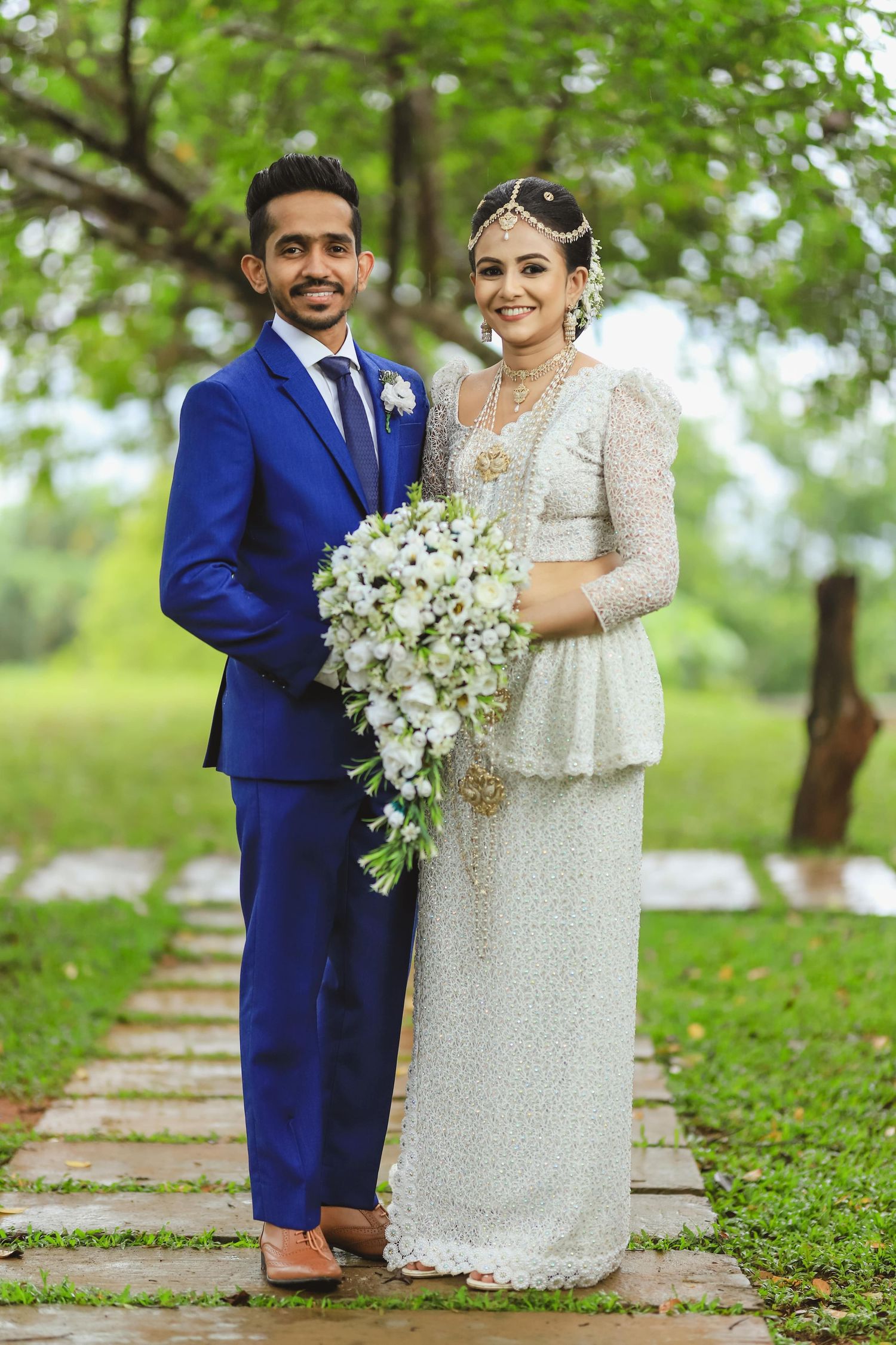 Romantic wedding portraits on stone pathway with couple in blue suit and white lace dress.