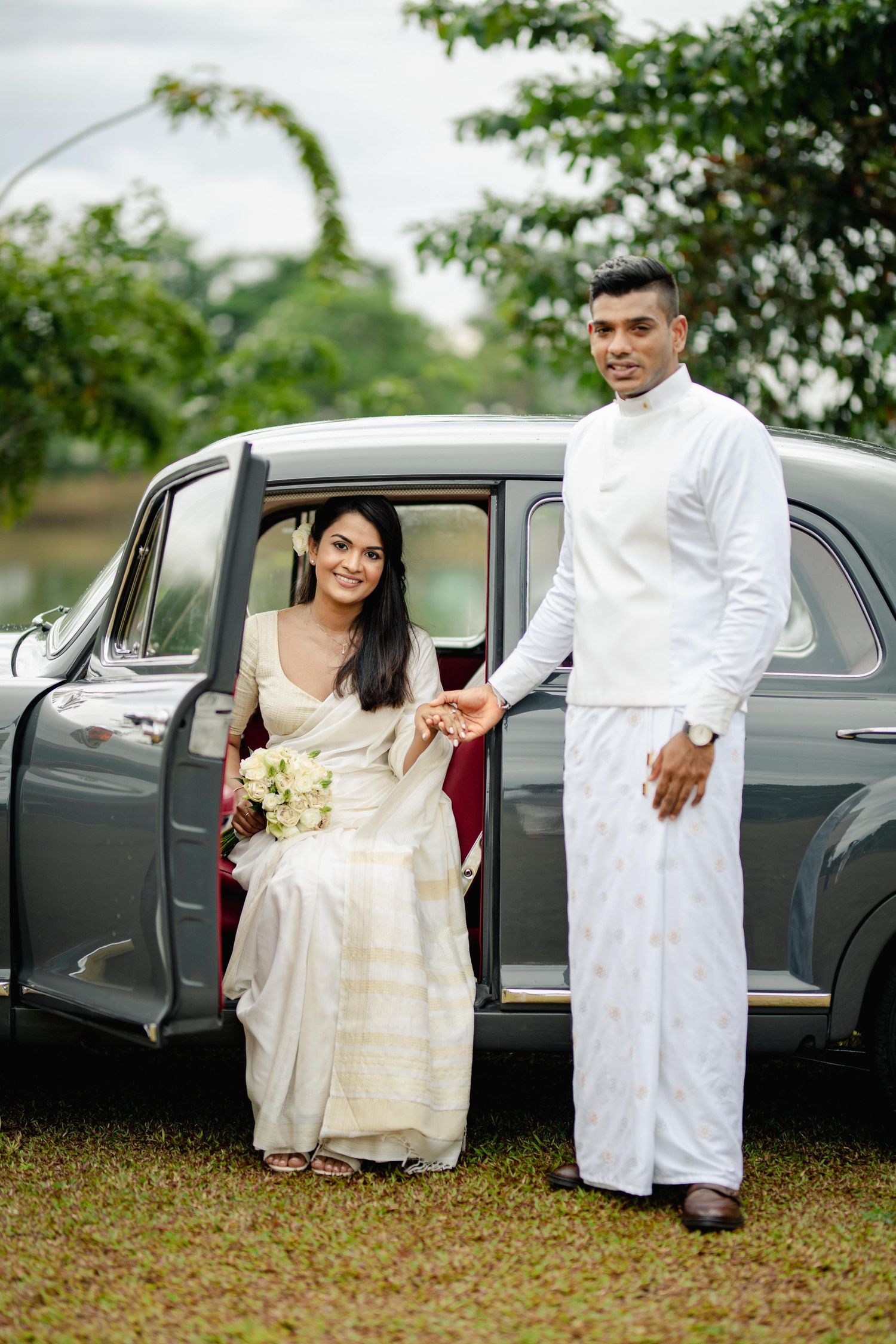 Classic vintage car parked on grass with people in formal attire beside it.