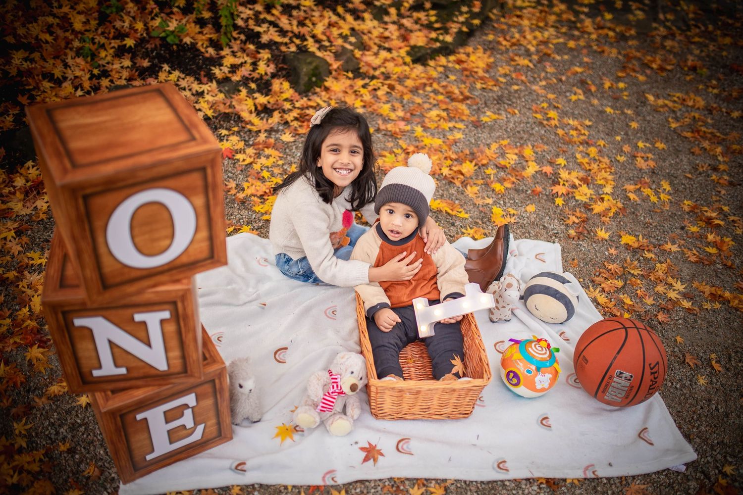 Autumn photo shoot with scattered leaves, decorative letters, and toys on white blanket.