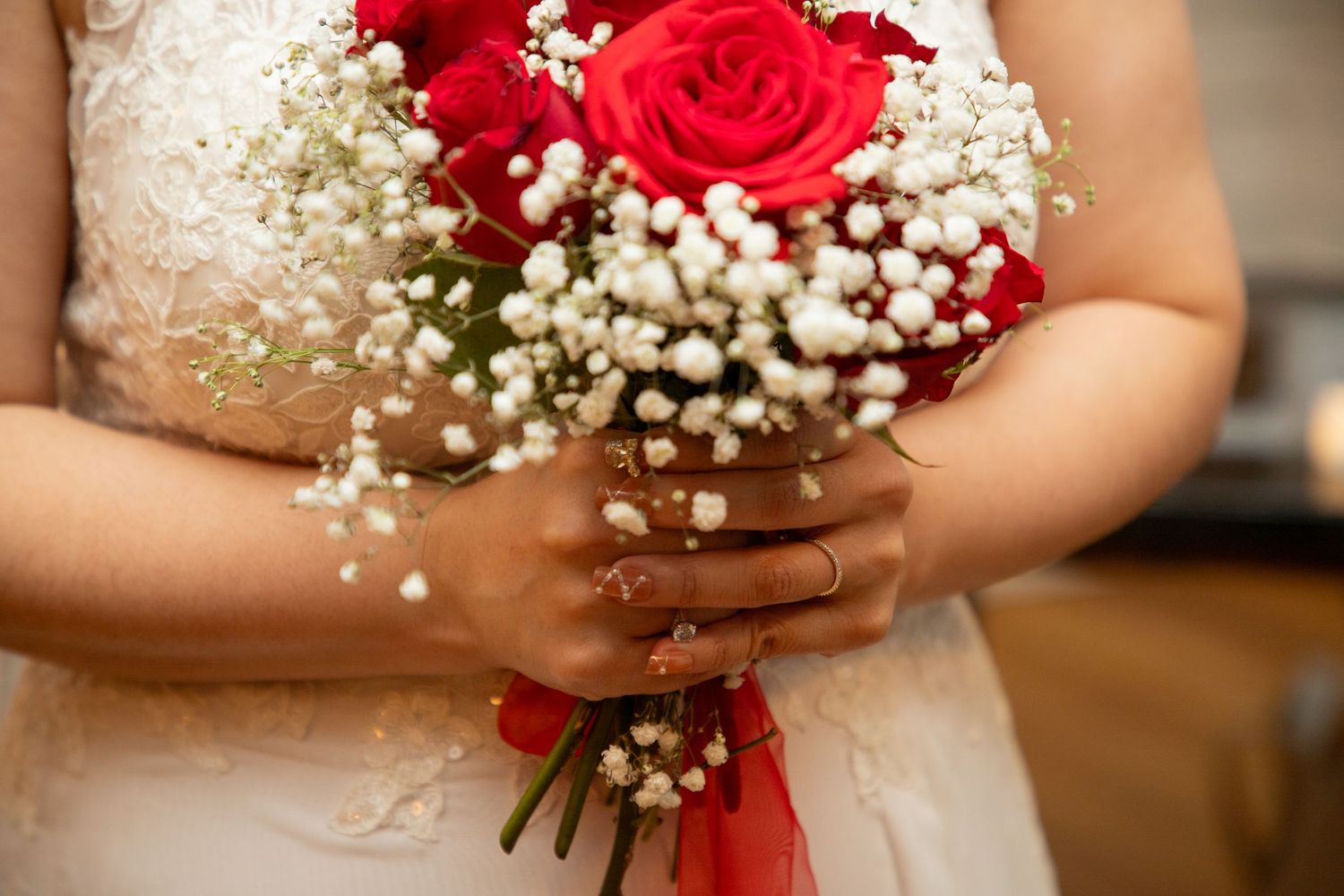 A close-up view of a bridal bouquet featuring vibrant red roses and delicate baby's breath flowers.