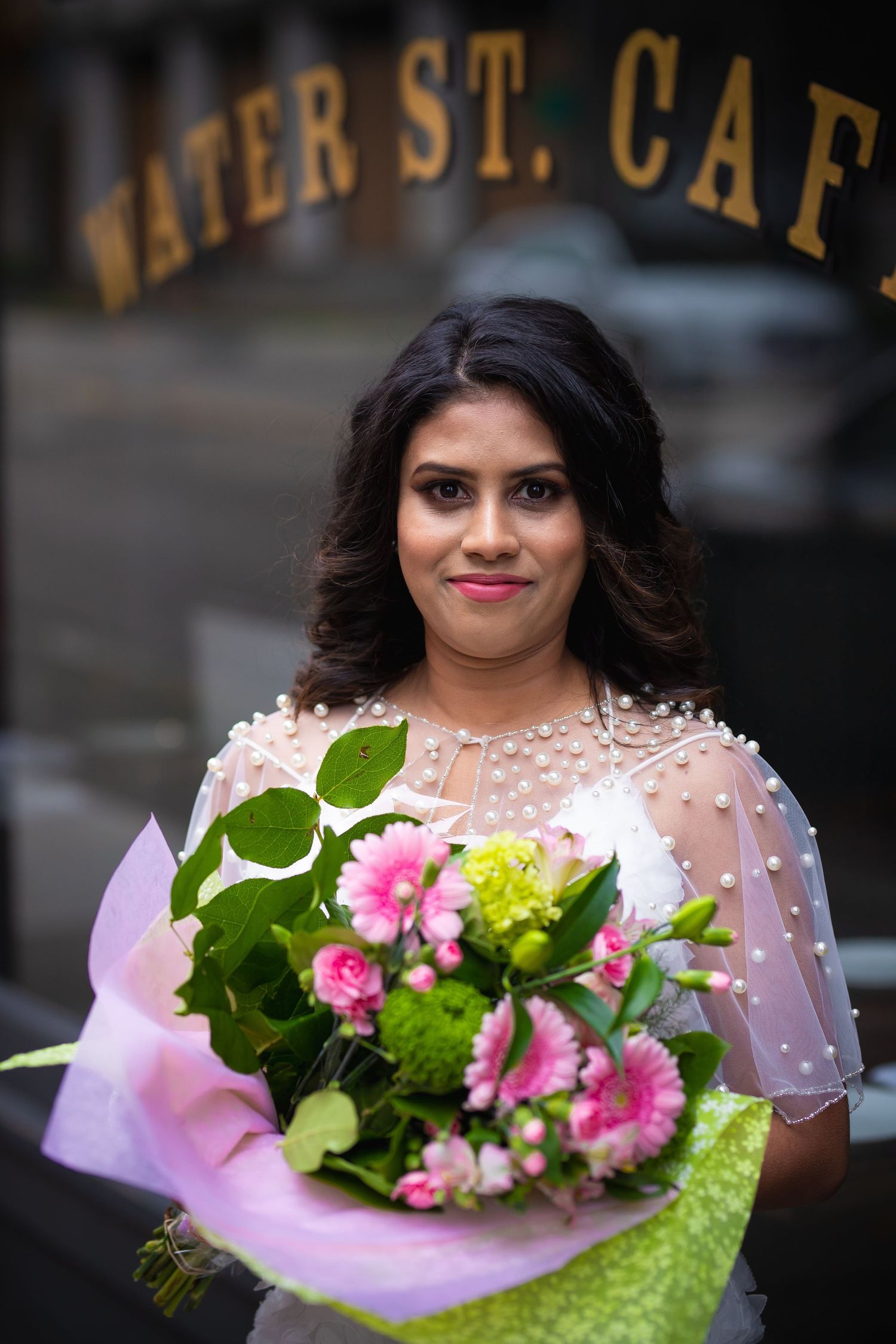 A person in a sheer dotted dress holds a vibrant pink and yellow floral bouquet against a dark background.