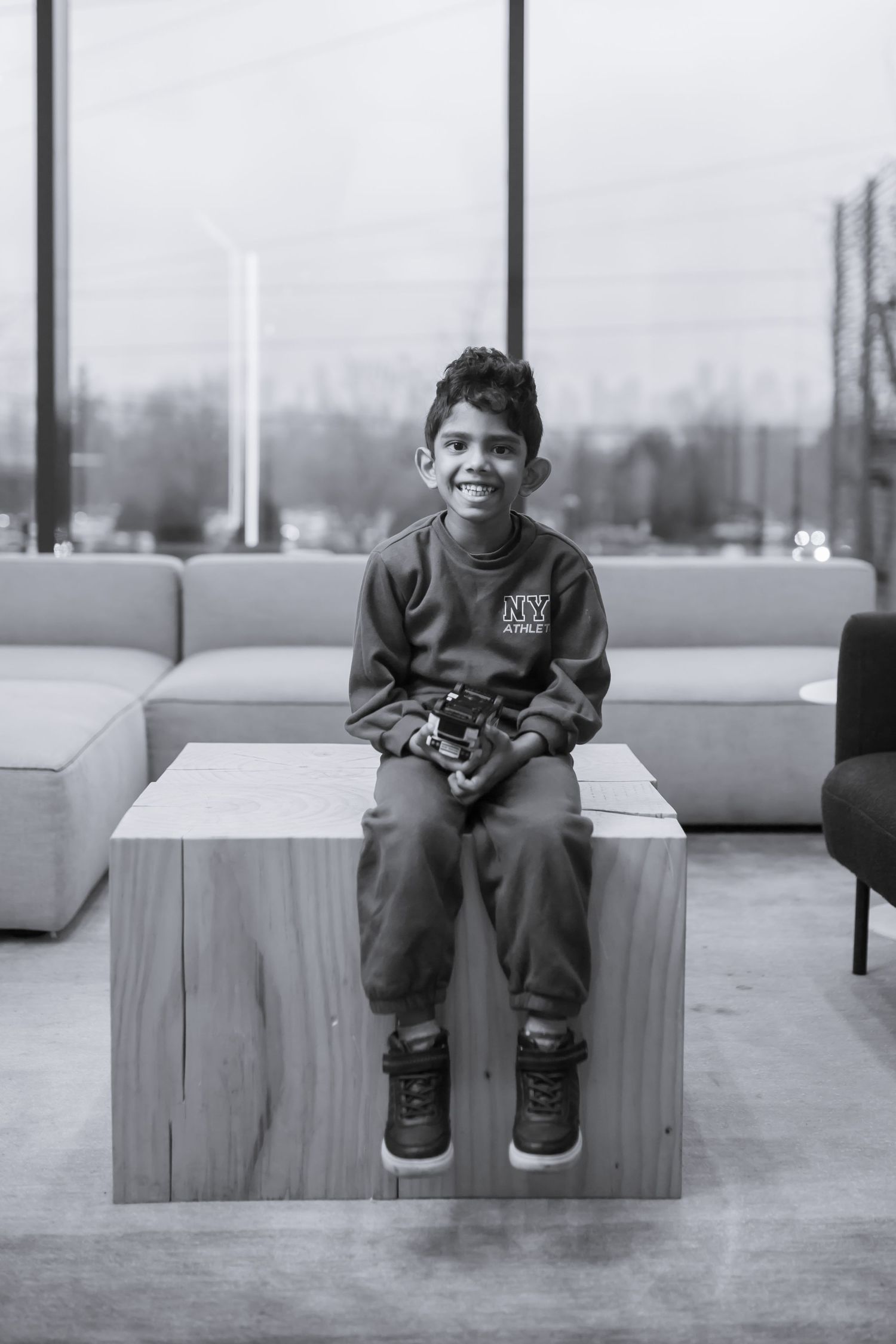 A black and white triptych shows a child sitting on a concrete bench in an urban setting.