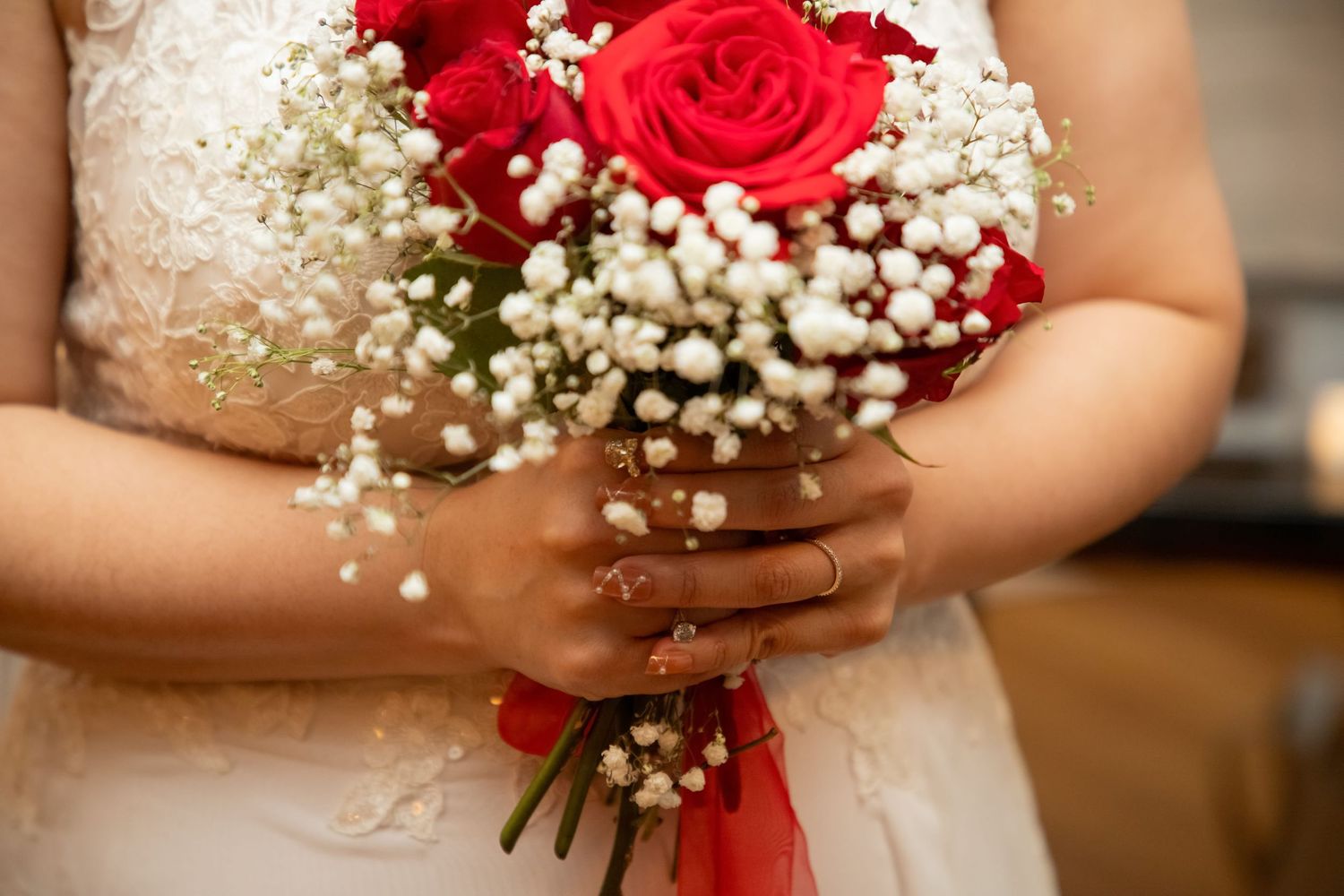 Close-up of bridal bouquet featuring vibrant red roses and delicate baby's breath flowers.