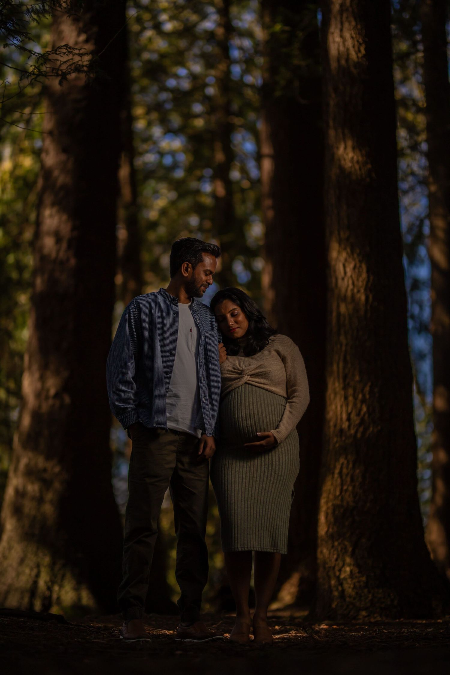 A couple shares an intimate moment among tall trees during golden hour.