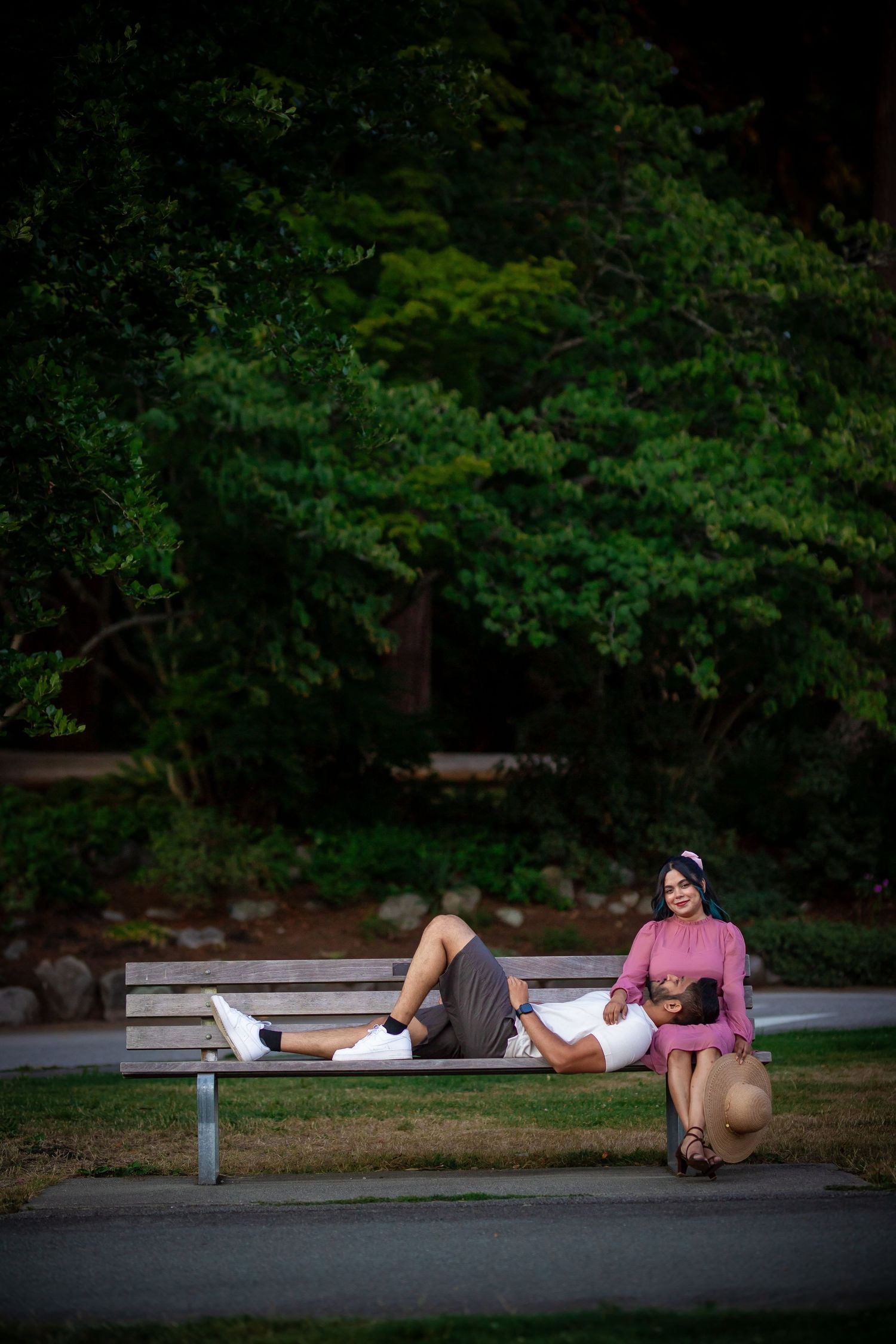 Two people relax casually on a bench against a dark green forest background.
